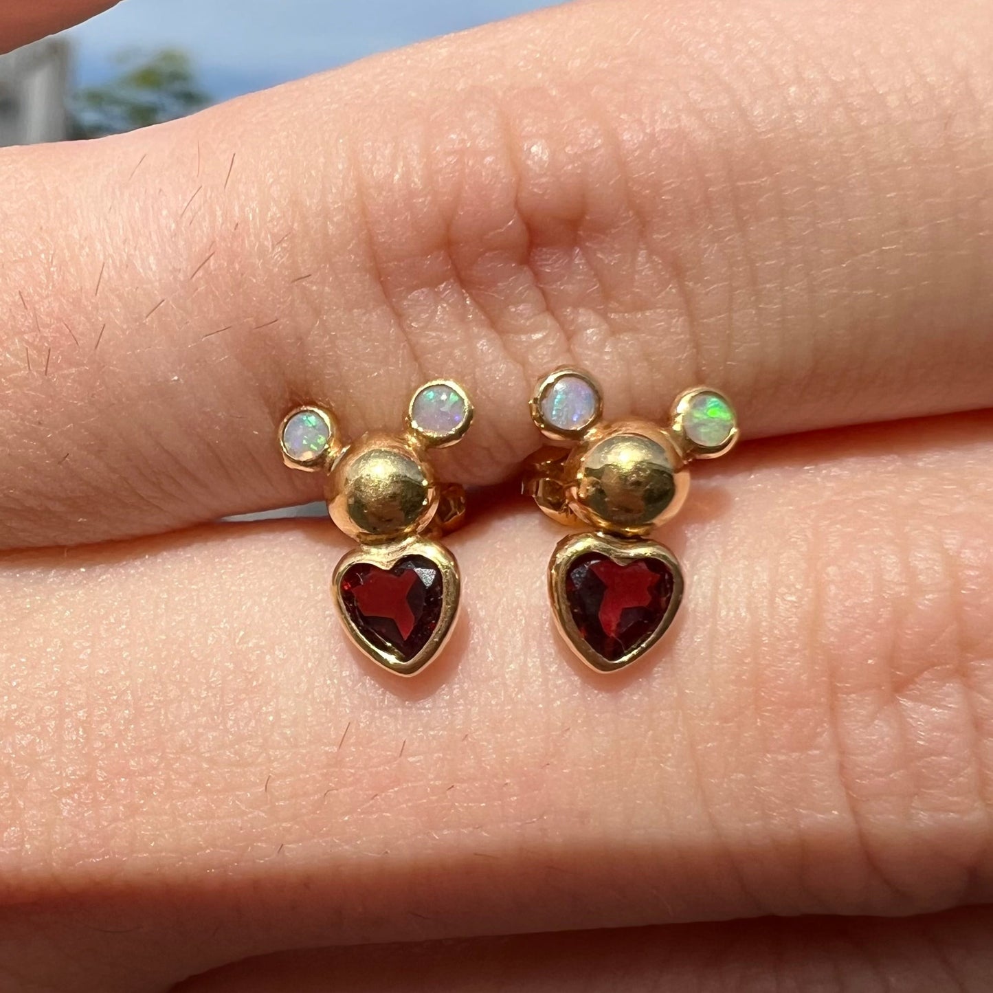 A pair of 18 karat yellow gold stud earrings set with two round fire opals and heart shaped garnets.