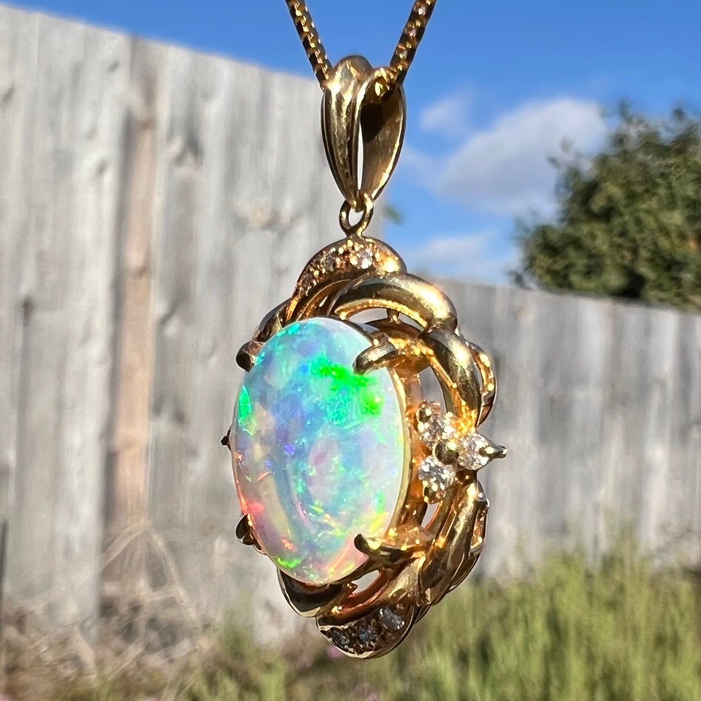 An 18k yellow gold crystal opal and diamond necklace. The opal is oval cut and has green/blue fire.