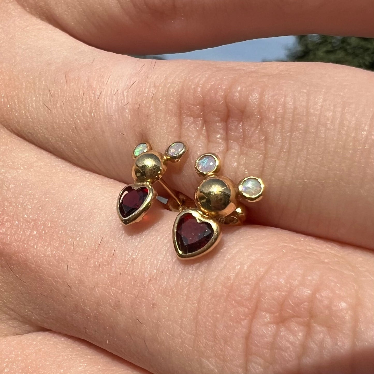 A pair of 18 karat yellow gold stud earrings set with two round fire opals and heart shaped garnets.