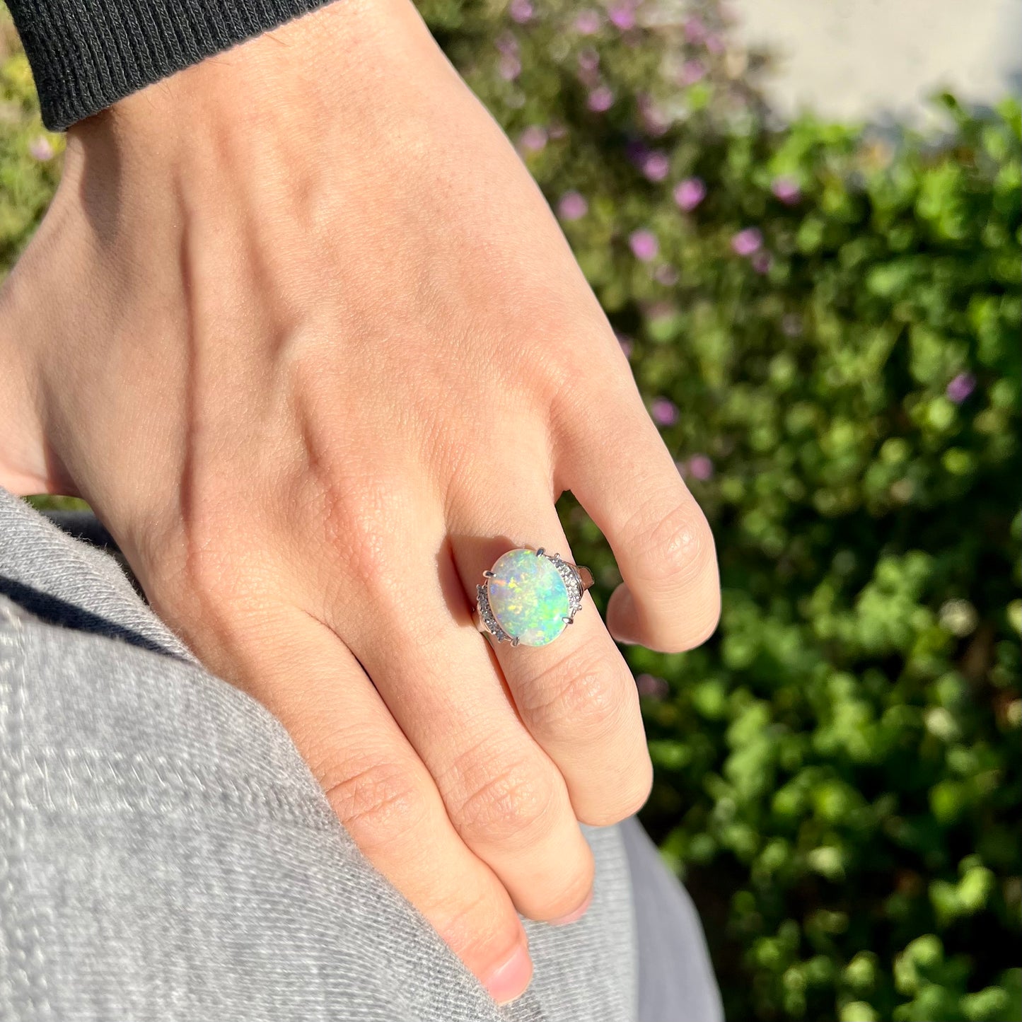 Close-up of hand resting on person's hip in sunlight wearing a 3.54ct Australian light opal ring, framed with diamond accents in platinum.