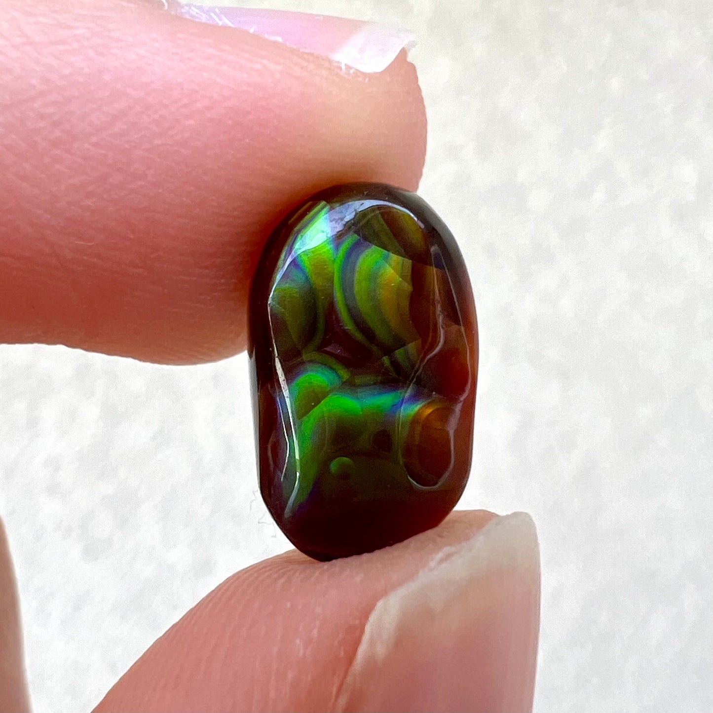 A loose, oval cabochon cut Mexican fire agate stone. The stone has multi-colored banding with blue overtones.