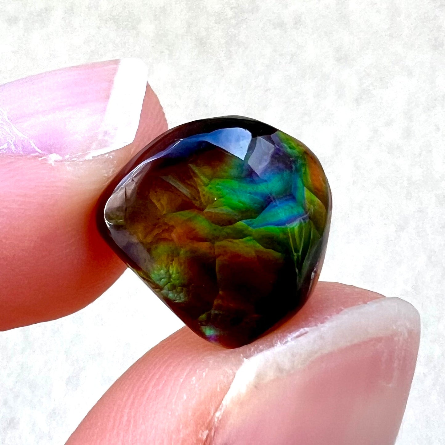 A freeform cabochon cut Mexican fire agate stone. The stone has a bright purple flash with green, yellow, and orange.