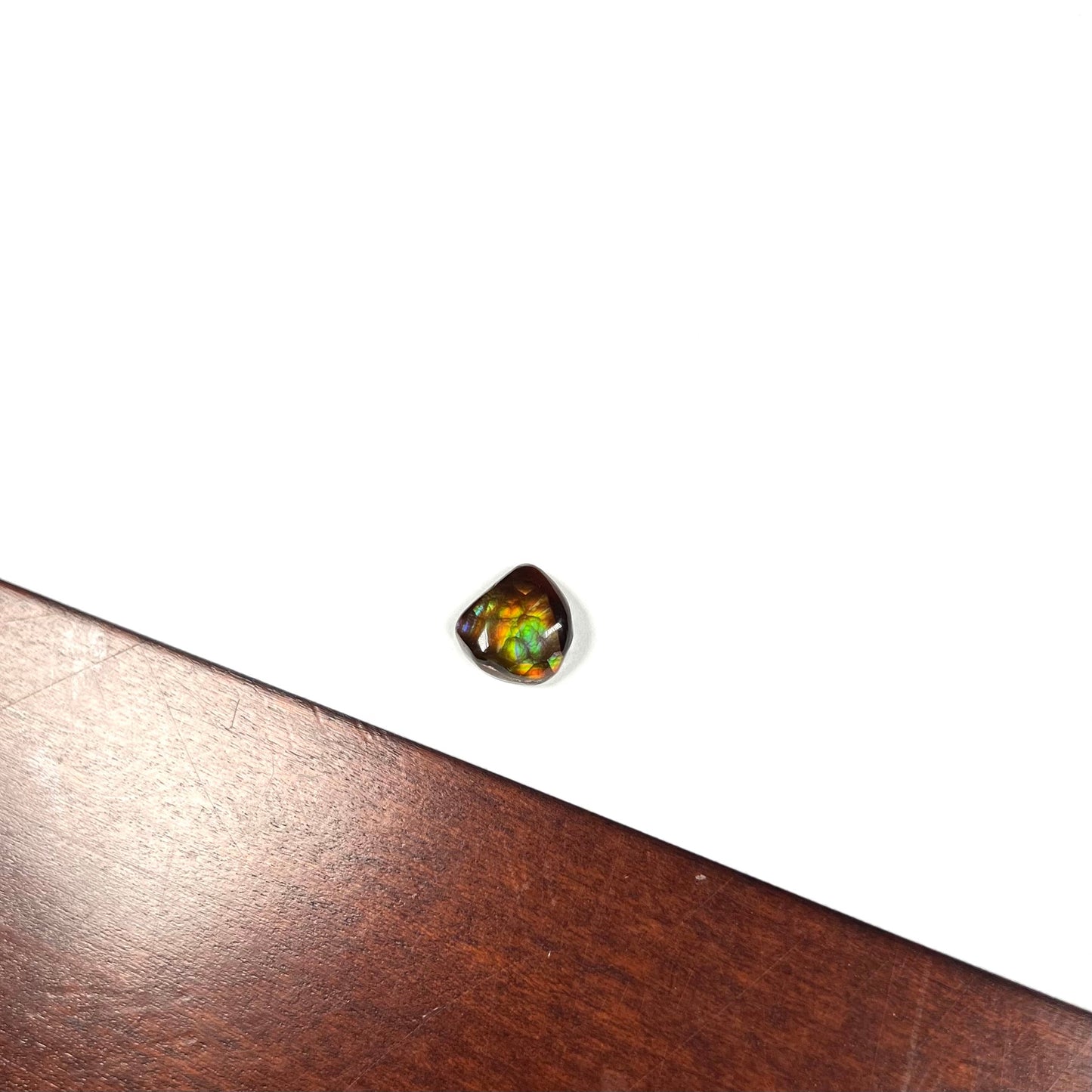 A freeform cabochon cut Mexican fire agate stone. The stone has a bright purple flash with green, yellow, and orange.