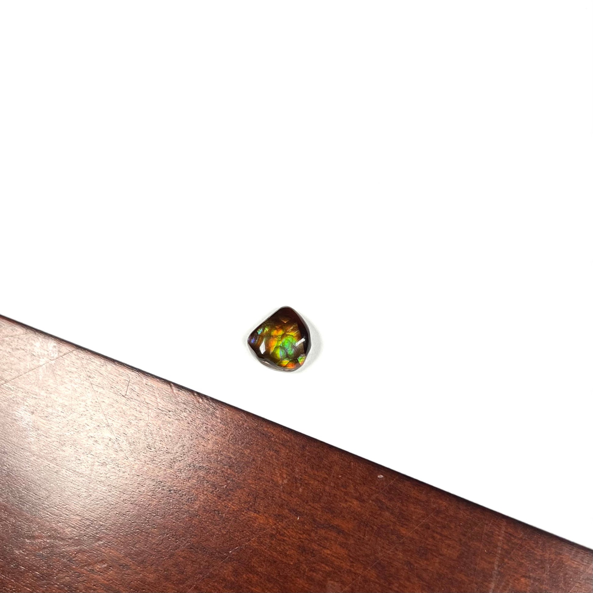 A freeform cabochon cut Mexican fire agate stone.  The stone has a bright purple flash with green, yellow, and orange.
