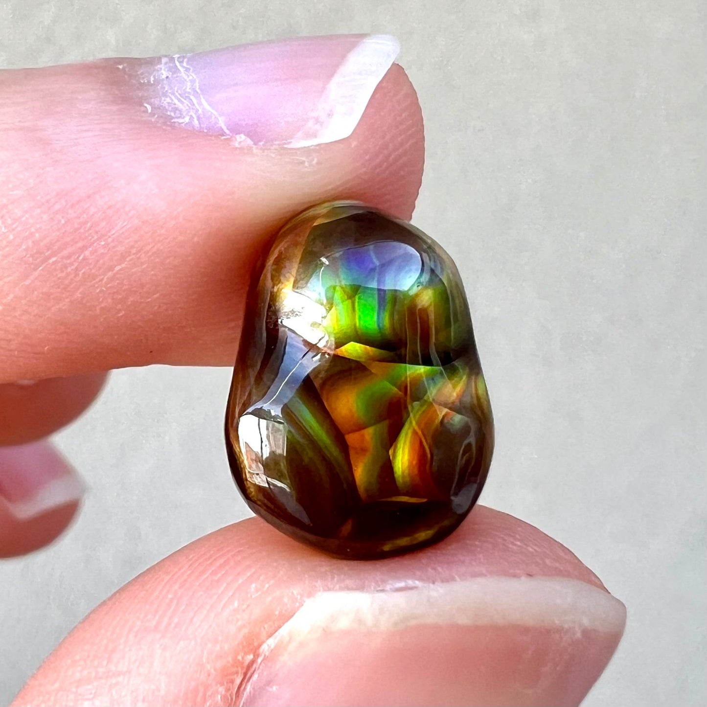 A loose, freefrom cabochon cut Mexican fire agate stone. The stone has red, green, yellow, and purple banding.