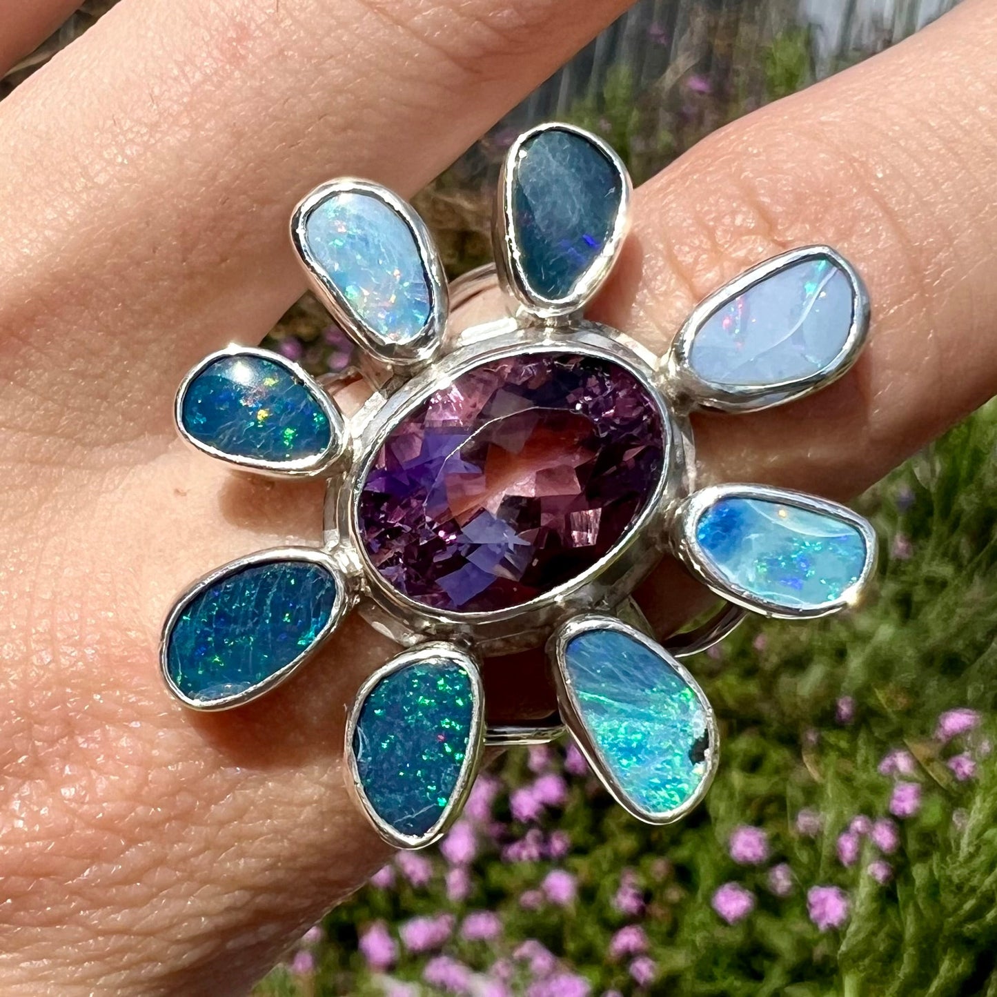 A sterling silver flower shaped ring set with an oval cut amethyst in the center and black opal doublet petals.