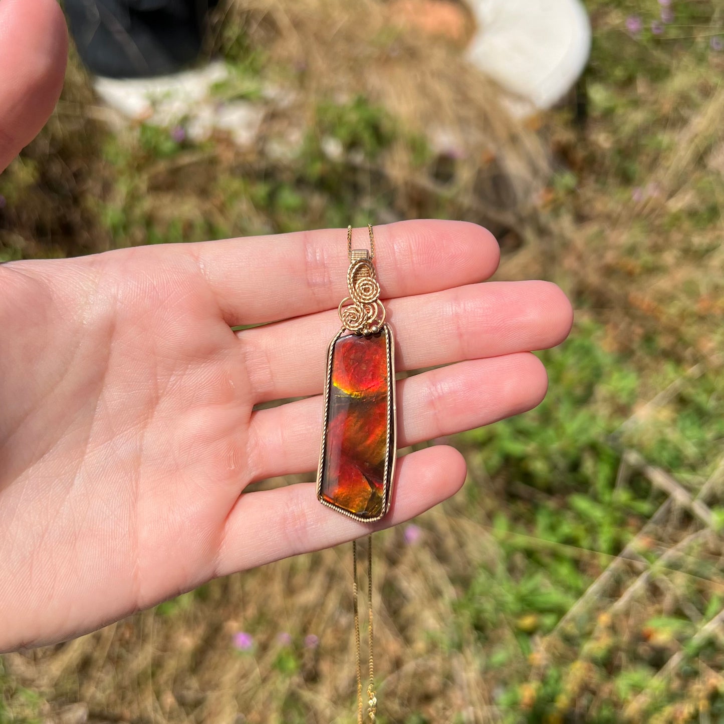 A red ammolite pendant held in a hand in the sunlight.