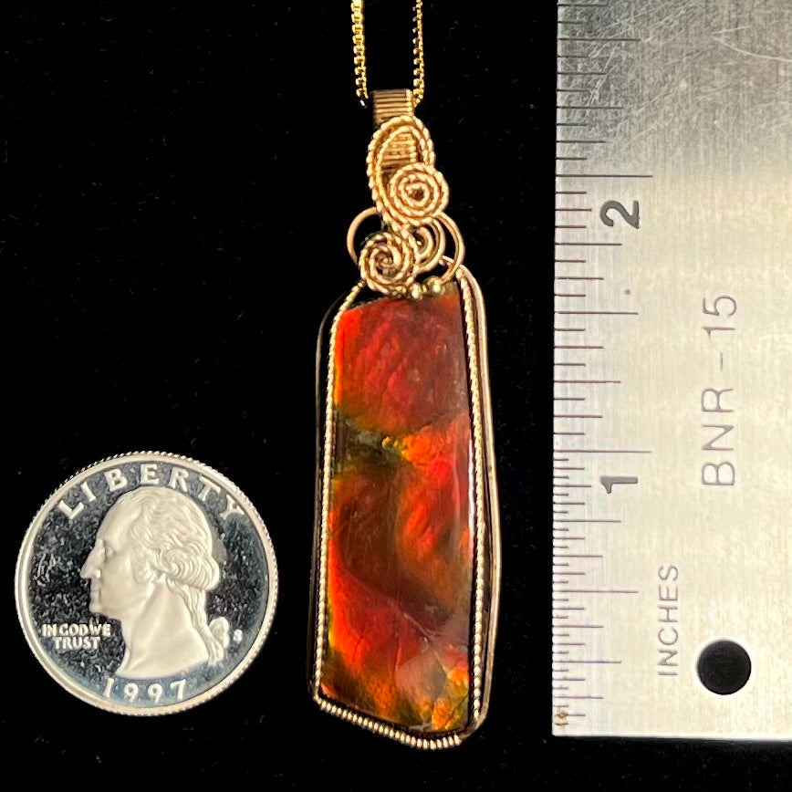 A red ammolite pendant next to a ruler and US quarter for scale. The pendant measures 2.25 inches.