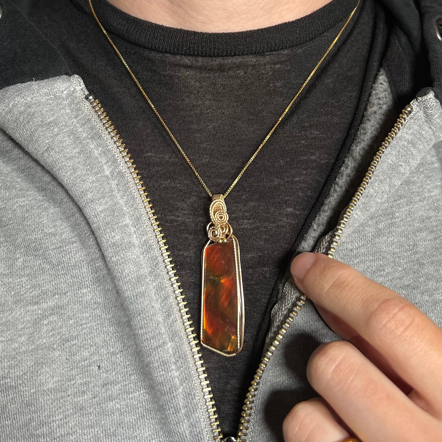 A gold filled wire wrapped ammolite necklace worn against a dark shirt in a partially unzipped jacket.