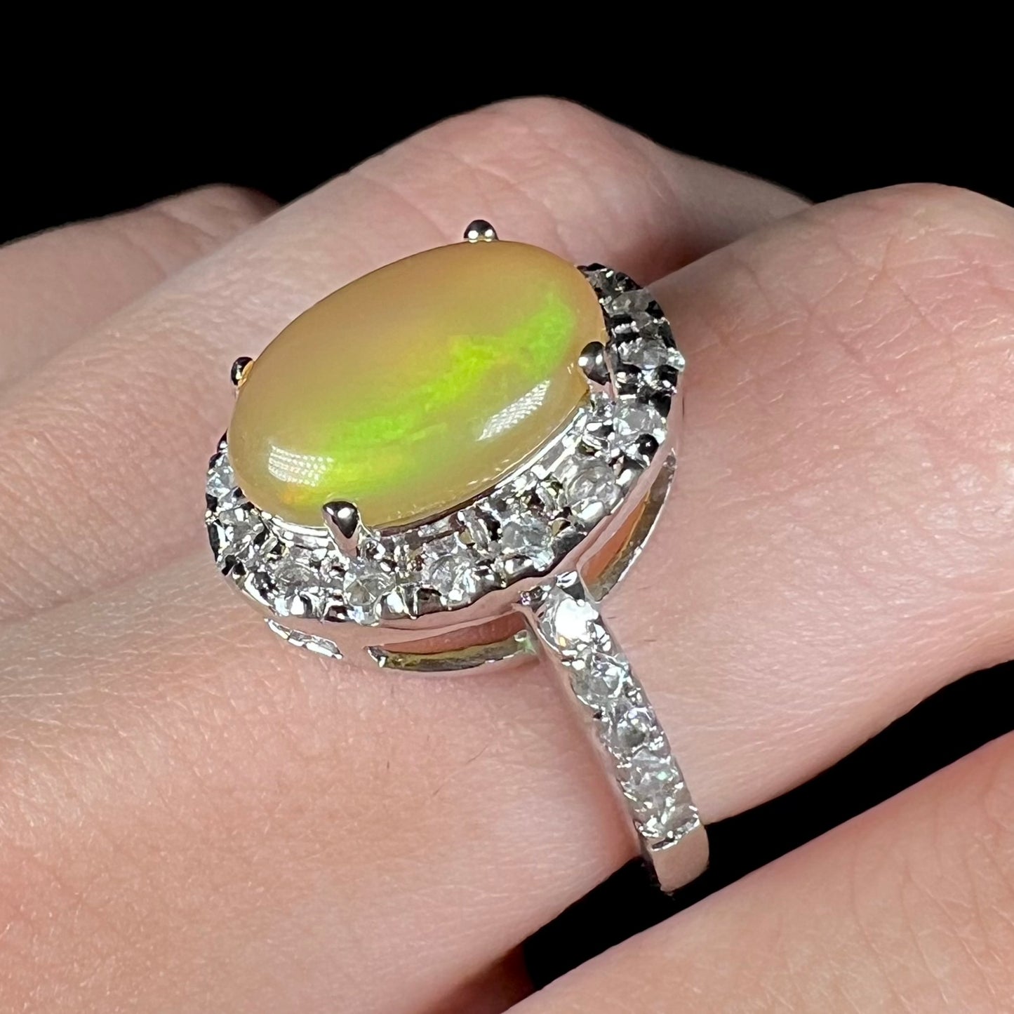 Angled close-up view of a sterling silver Ethiopian fire opal ring with a CZ halo, worn on a finger.