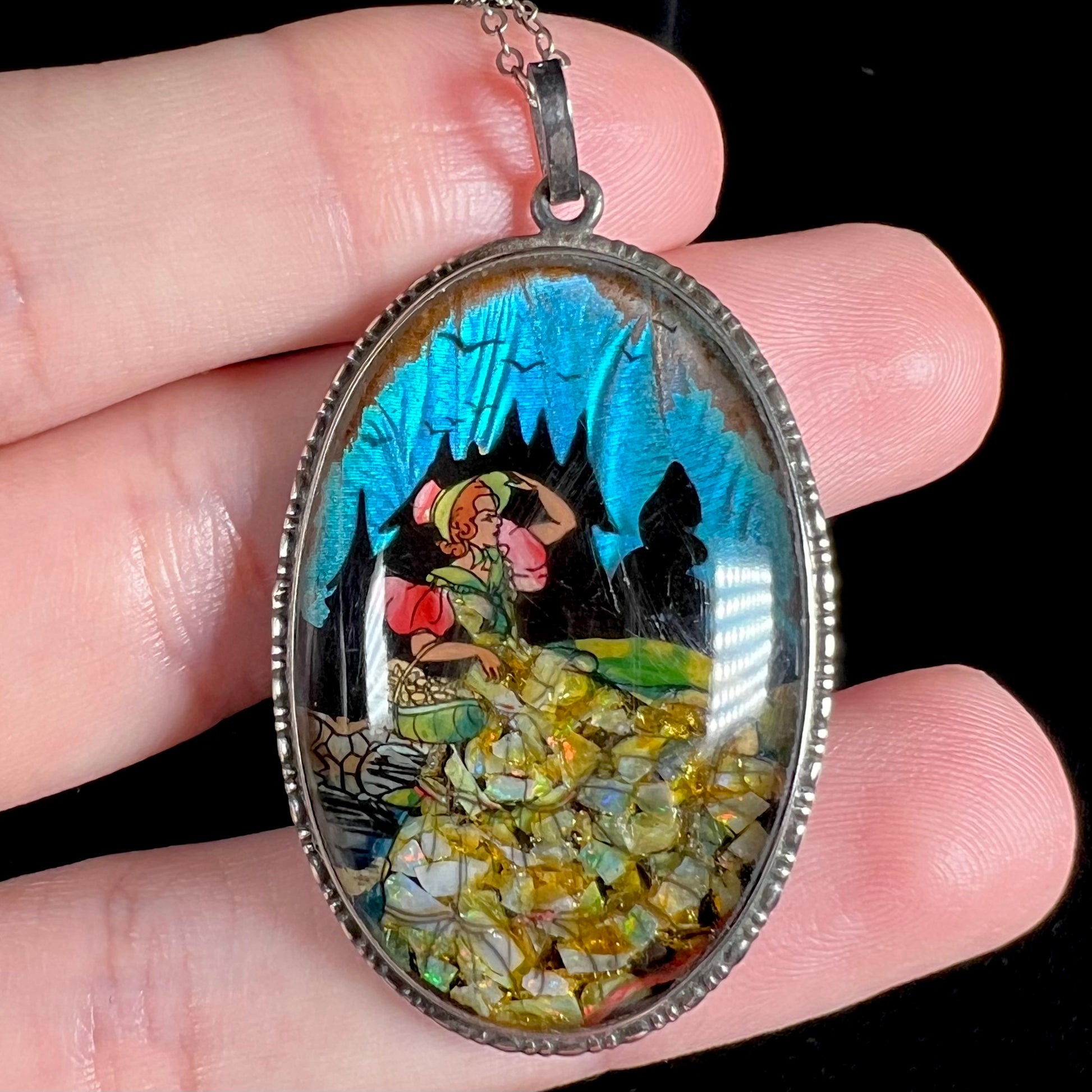 An antique butterfly wing pendant with crushed opal, shown close-up in a hand against a black backdrop.