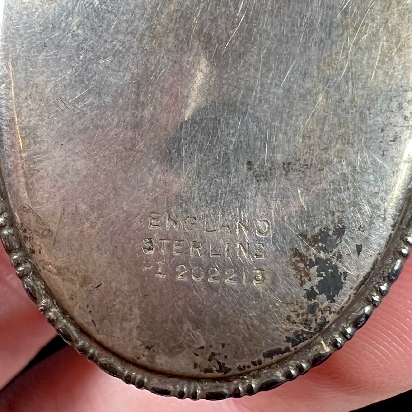 Close-up of the hallmarks on the back of a silver pendant that reads, "ENGLAND", "STERLING", and "PI 202213".