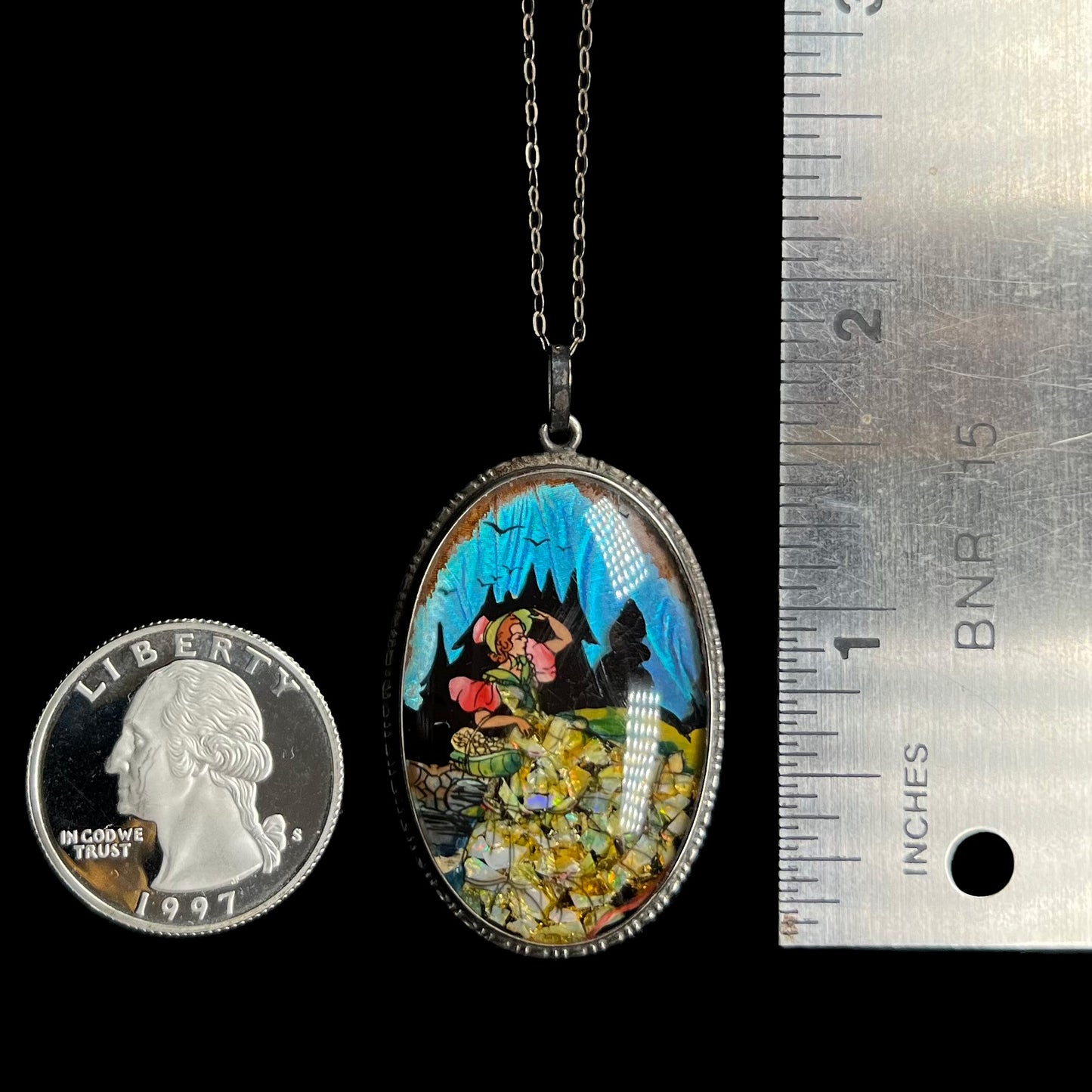 An antique crushed opal and butterfly wing pendant, shown next to a quarter and ruler.  The pendant measures 1.75 inches.