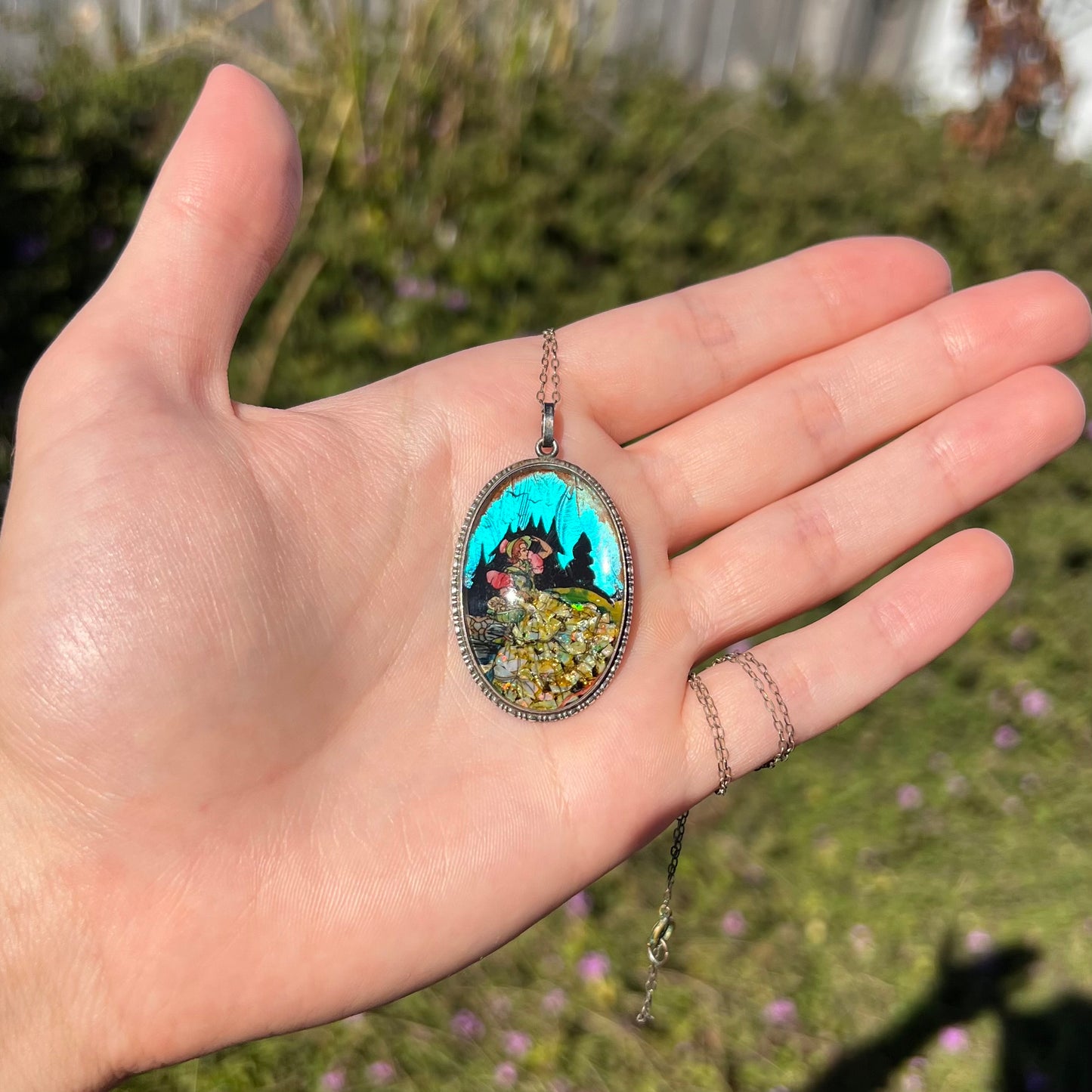 An antique silver butterfly wing and opal pendant shown in a hand in sunlight, the butterfly wing glows blue.