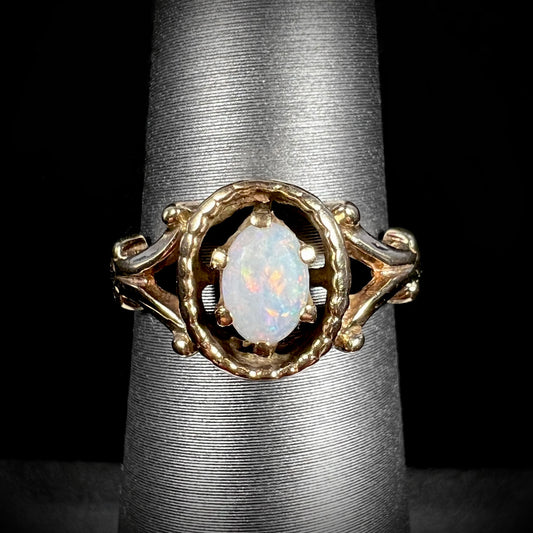 A ladies' Art Nouveau style opal solitaire ring.  The mounting is yellow gold with filigree accents.