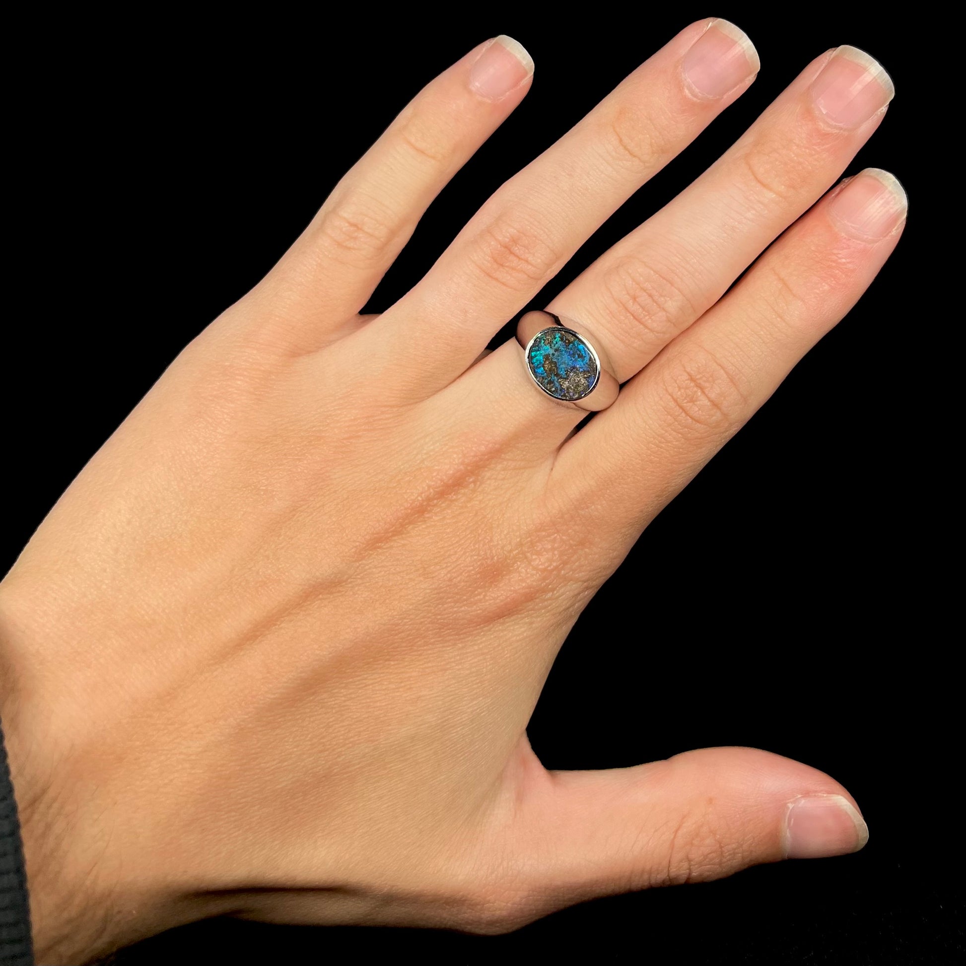 A stainless steel men's Australian boulder opal ring with blue color play, shown on a hand against a black backdrop.