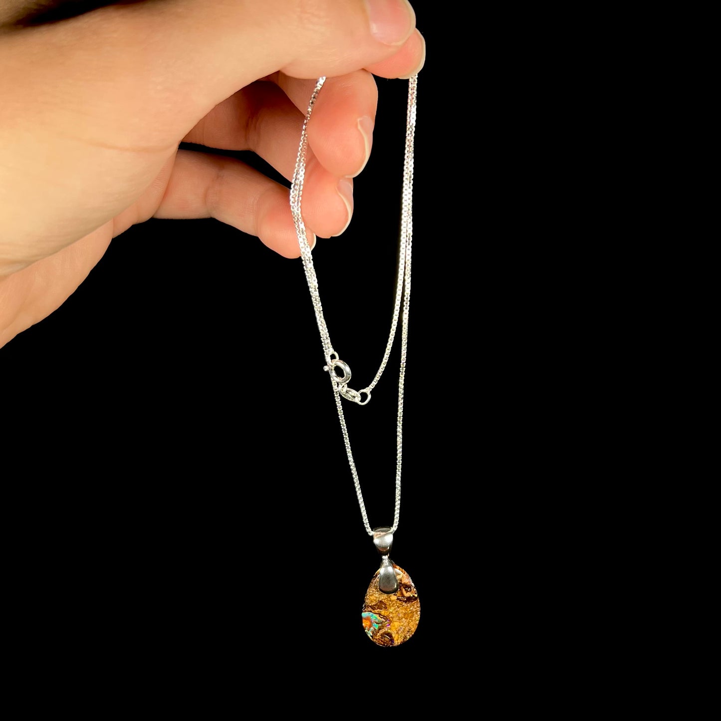 An Australian boulder opal necklace with a sterling silver bail. The opal has a greenish blue flash of color.