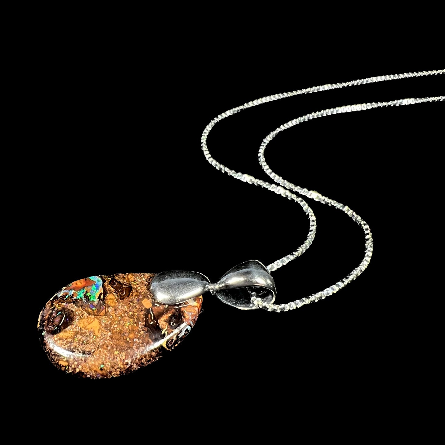 An Australian boulder opal necklace with a sterling silver bail. The opal has a bright green flash of color.