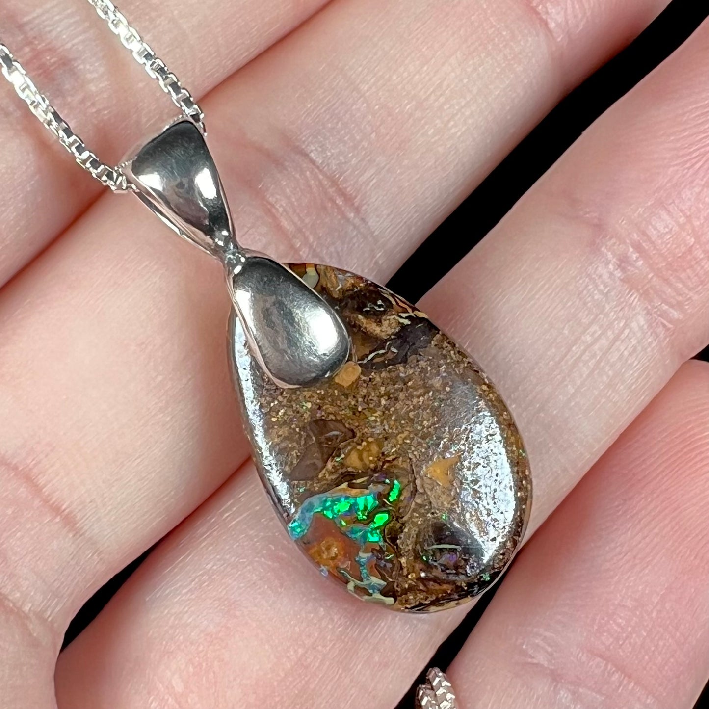 An Australian boulder opal necklace with a sterling silver bail. The opal has a bright green flash of color.