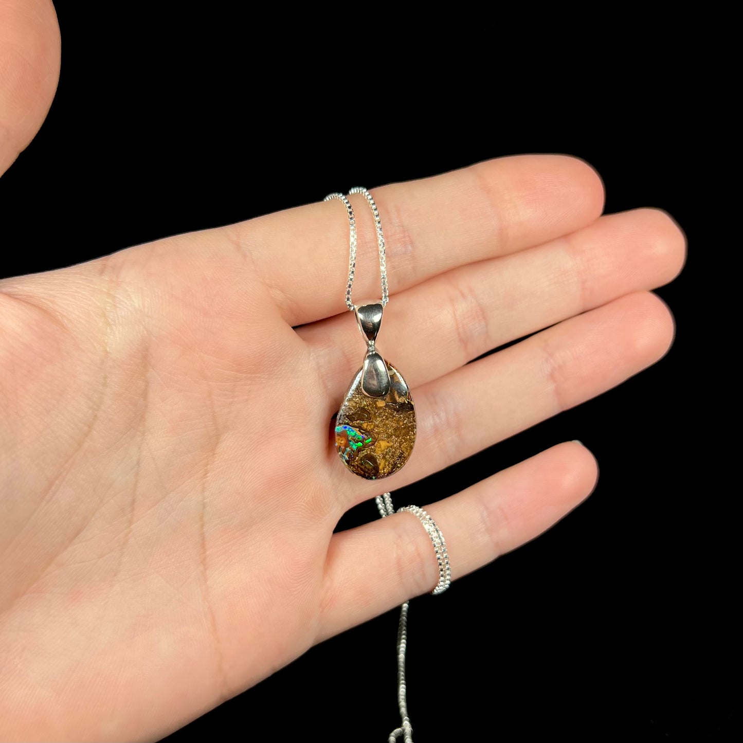 An Australian boulder opal necklace with a sterling silver bail. The opal has a bright green flash of color.