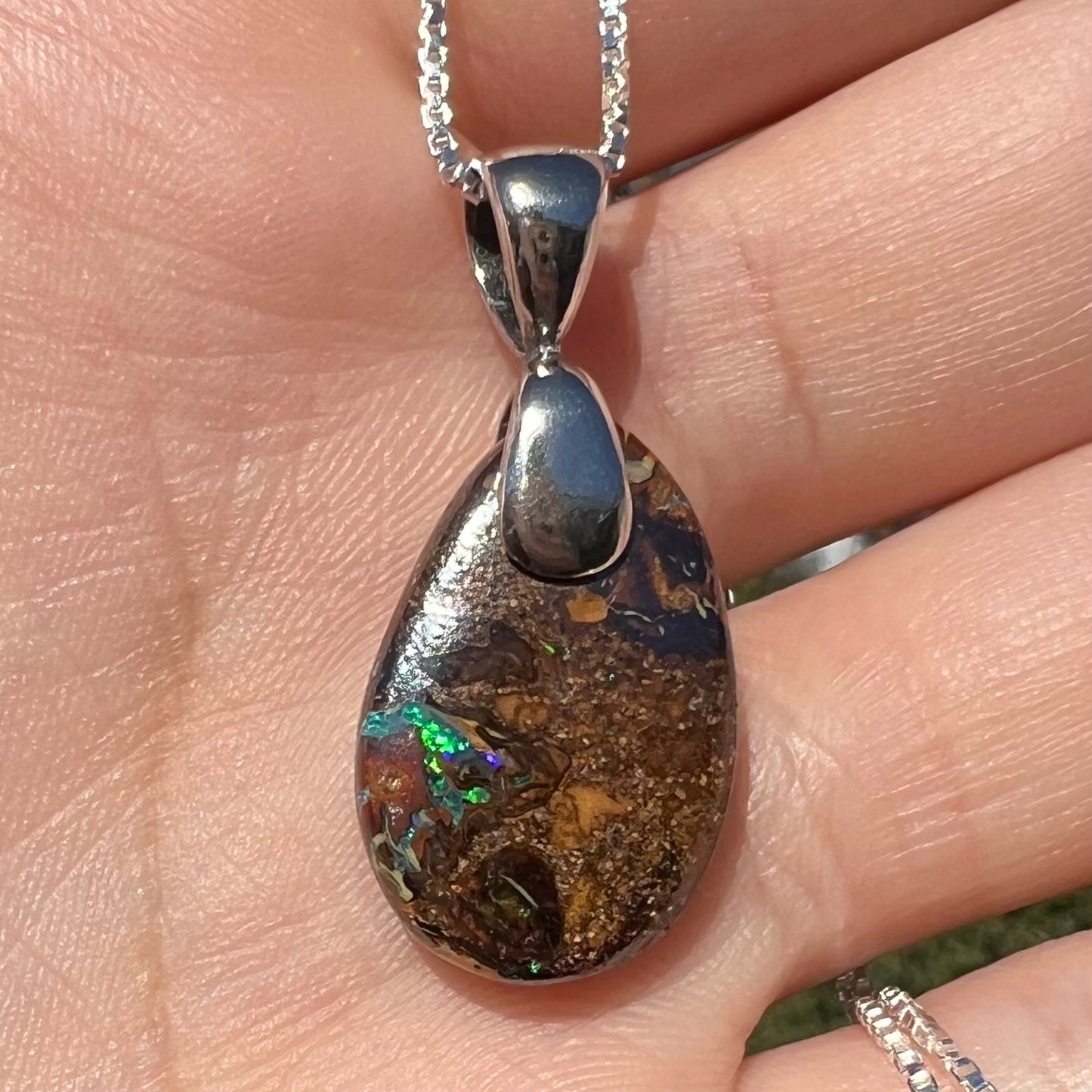 An Australian boulder opal necklace with a sterling silver bail. The opal has a bright green flash of color.