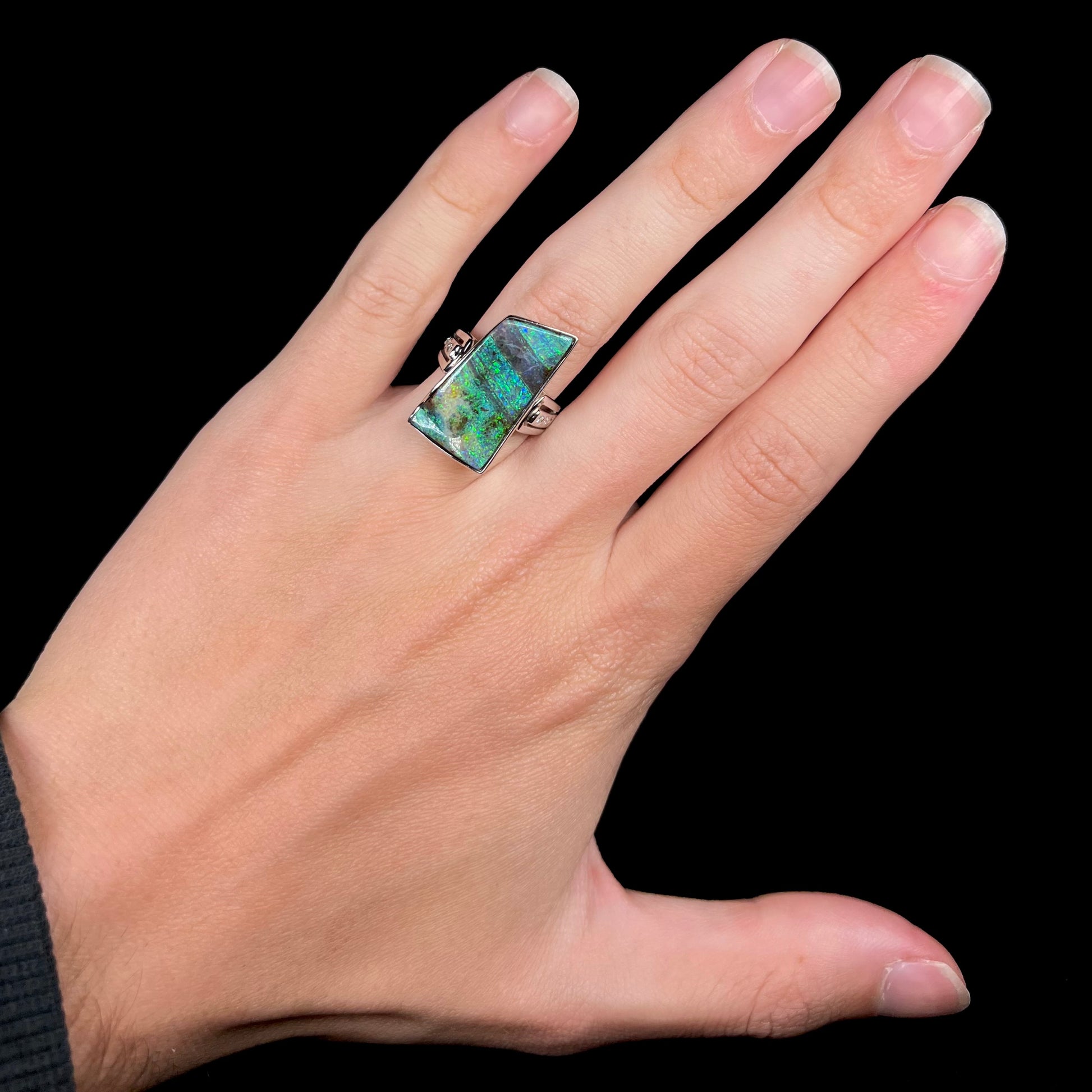 A blue and green striped Australian boulder opal ring in platinum, worn on a hand against a black background.