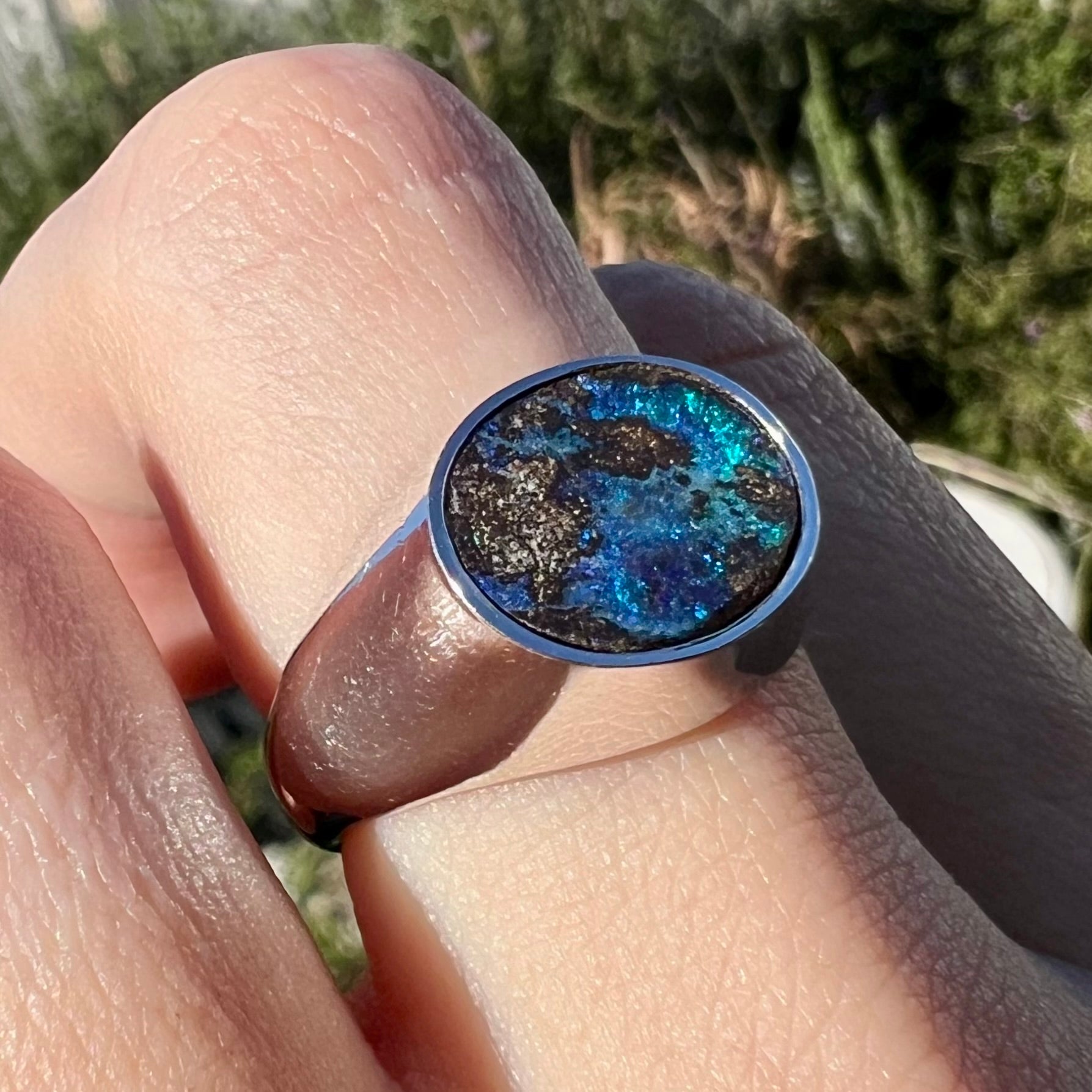 Angled close-up view of a stainless steel men's Australian boulder opal ring with blue color play shown in sunlight.