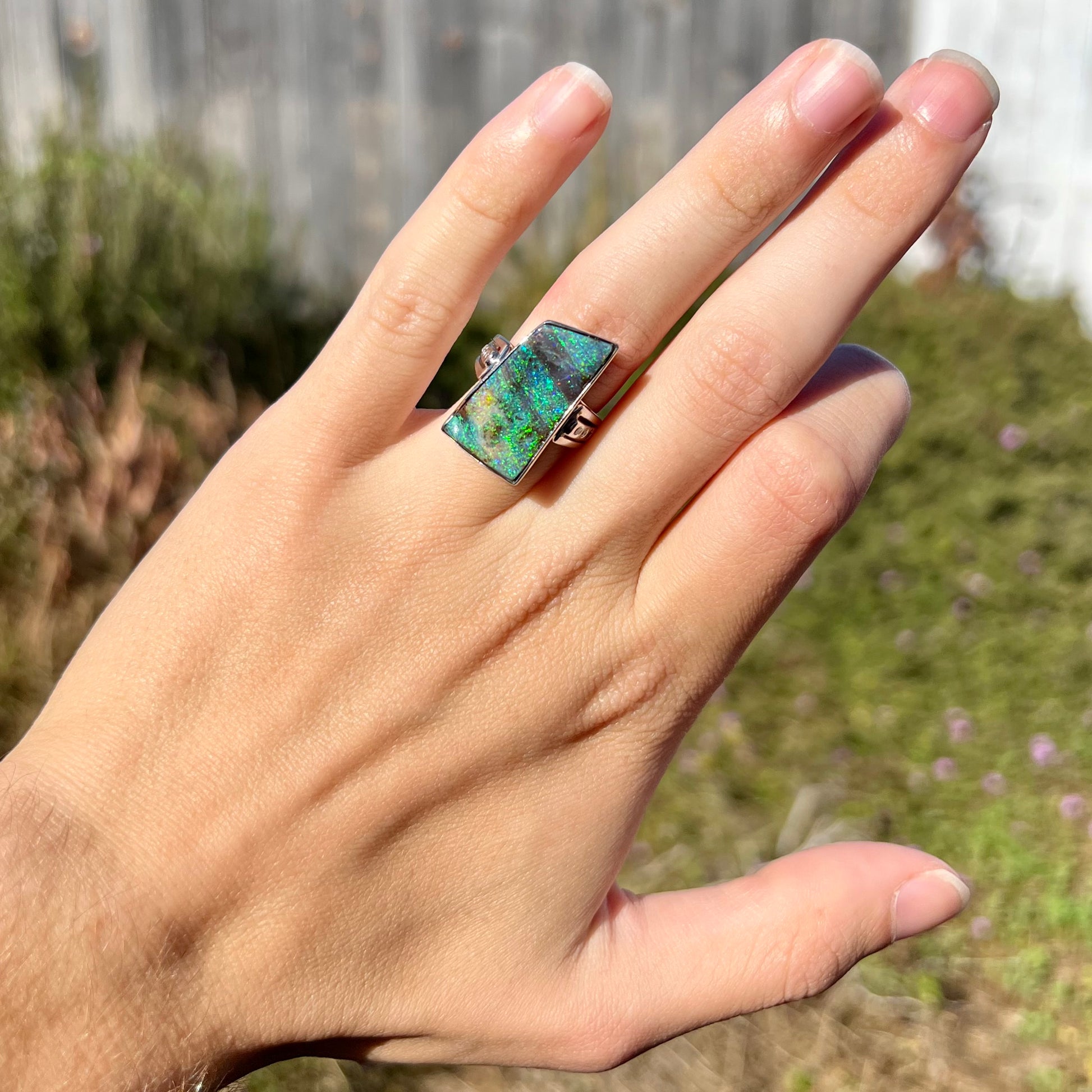 An Australian boulder opal statement ring with green color play in platinum, worn on a hand in sunlight.