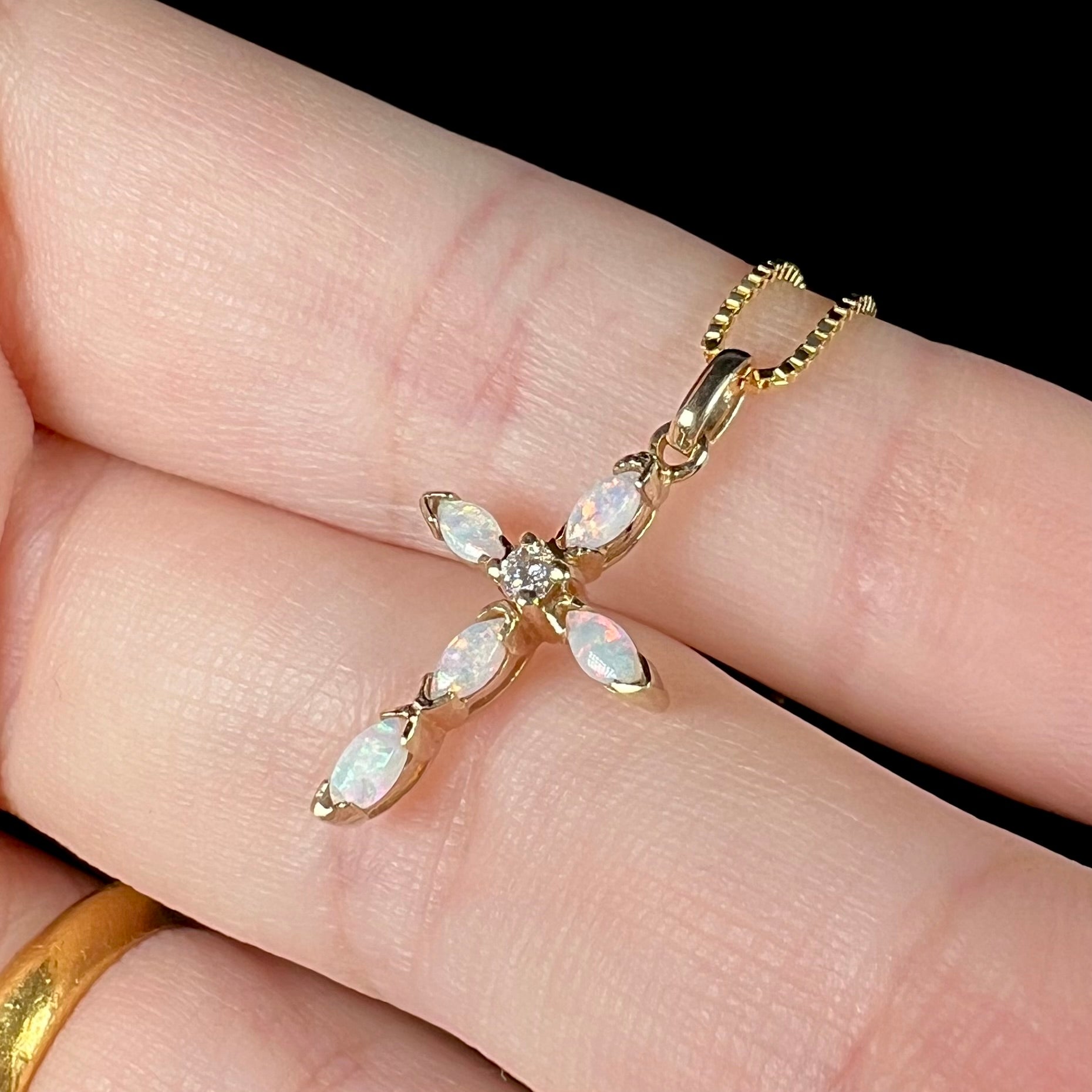 An Australian opal cross necklace held in two fingers, shown close-up at an angle.