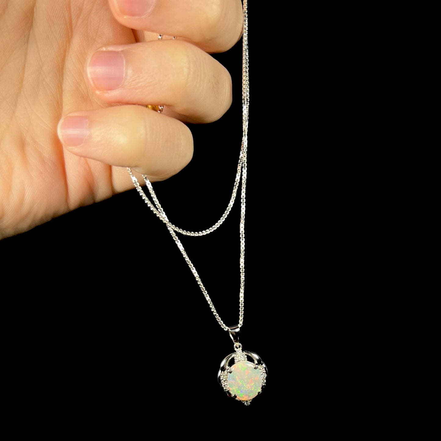 An Australian opal and diamond necklace, dangling from its chain by a hand.