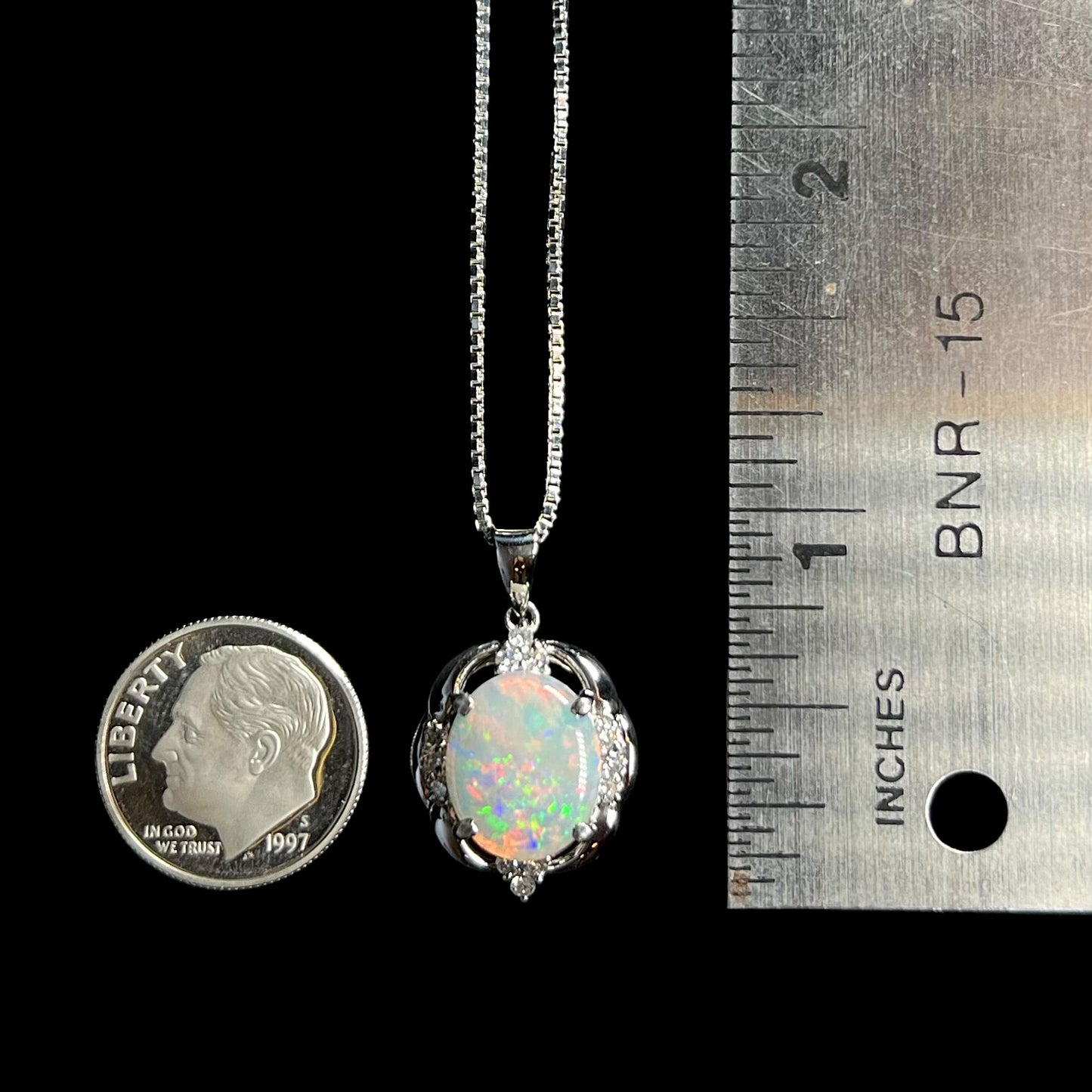An Australian opal and diamond necklace made from platinum next to a dime coin and ruler for scale.
