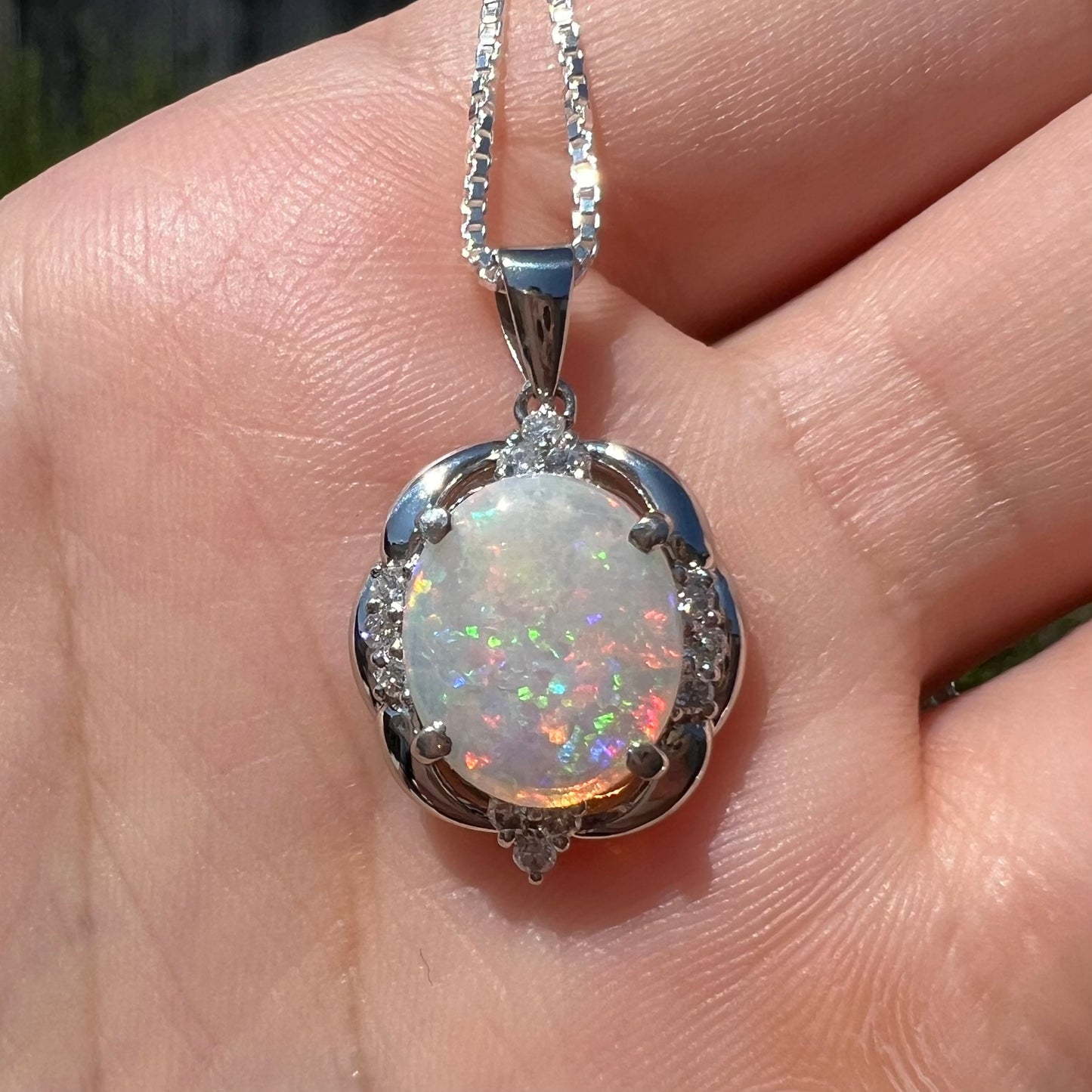 Close-up front view of an Australian opal and diamond necklace made from platinum, shown in the sunlight on a hand.