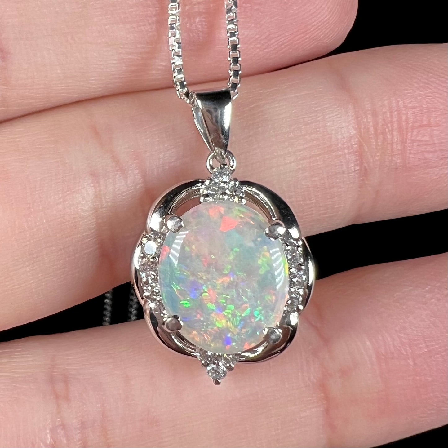 Close-up view of an Australian opal and diamond pendant shown in a hand from the front.