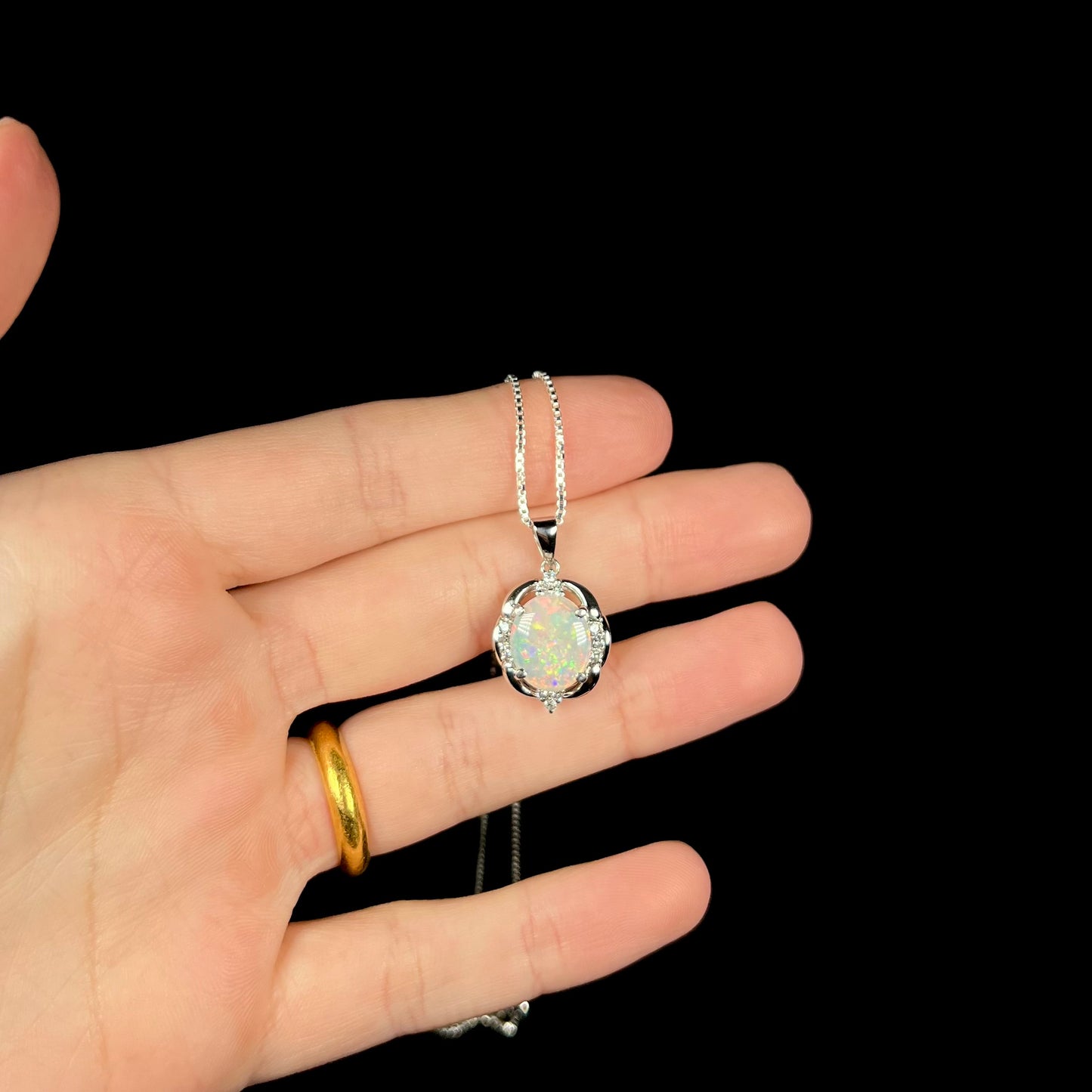 A platinum Australian opal and diamond pendant, held in a hand against a black background.