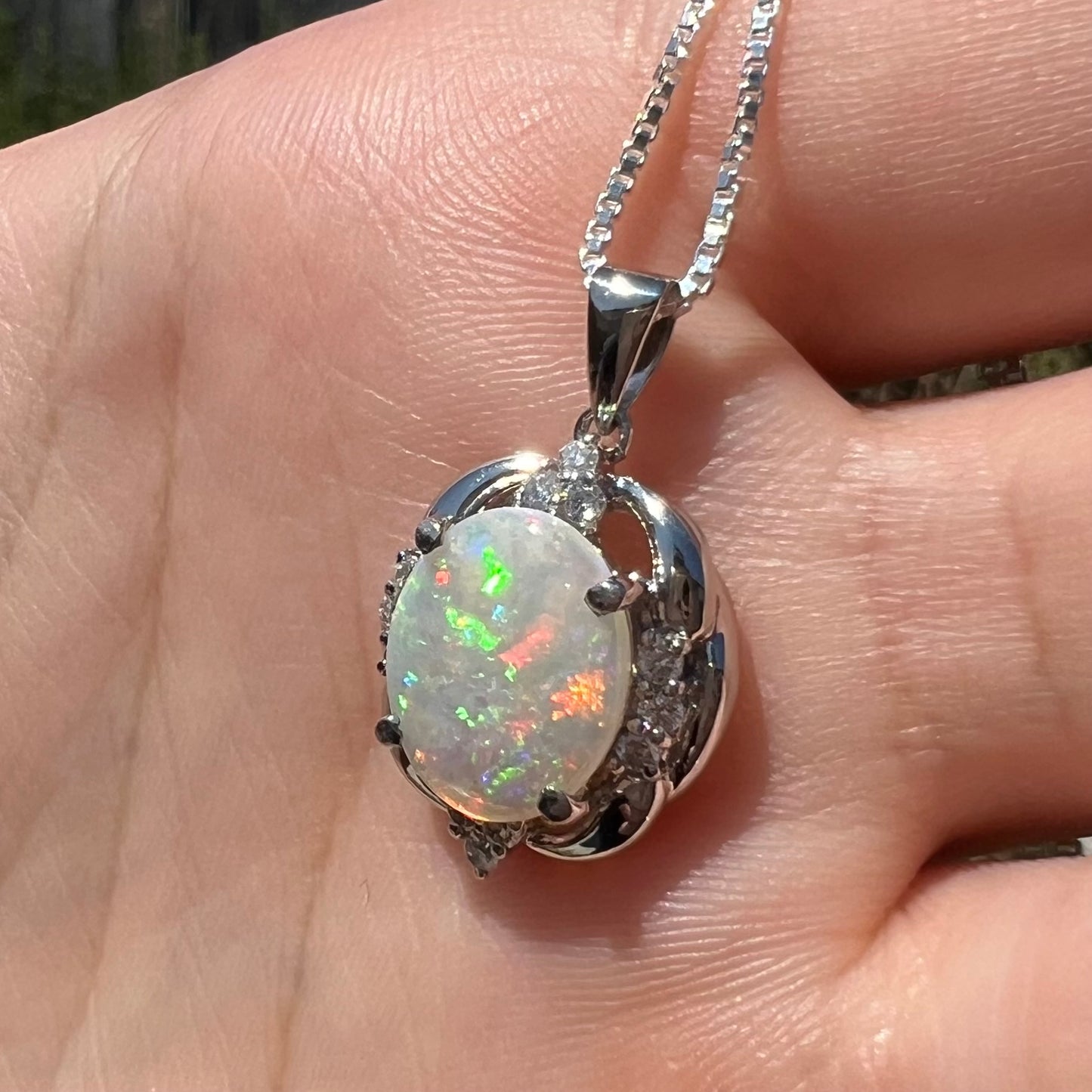A platinum Australian opal and diamond pendant on a silver chain, shown at an angle in the sunlight.