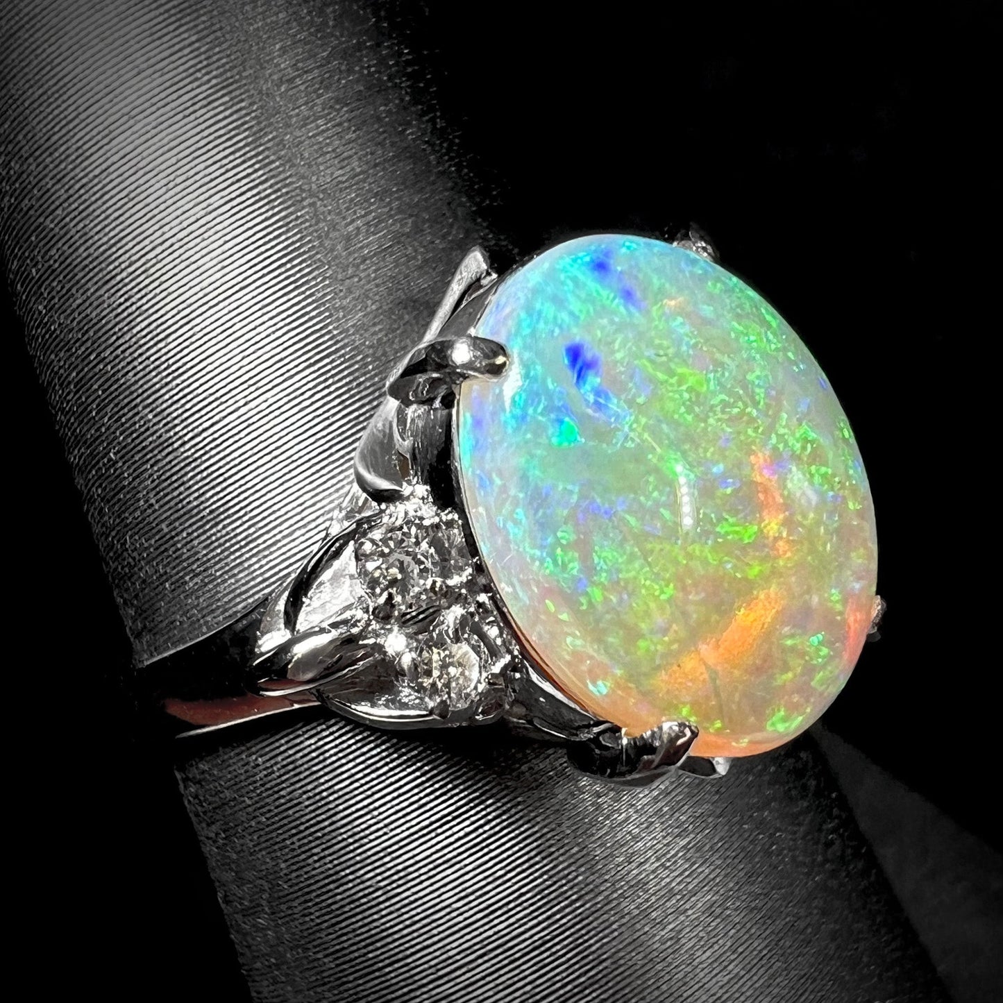 An Australian crystal opal and diamond engagement ring set in a platinum filigree mounting. The opal plays green/blue colors and has a crack.