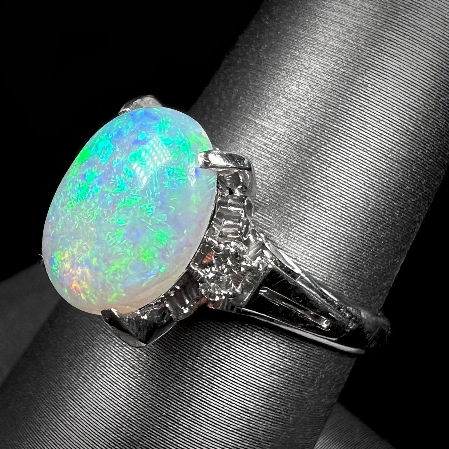A platinum filigree opal engagement ring set with diamond accents. The opal has green-blue colors.