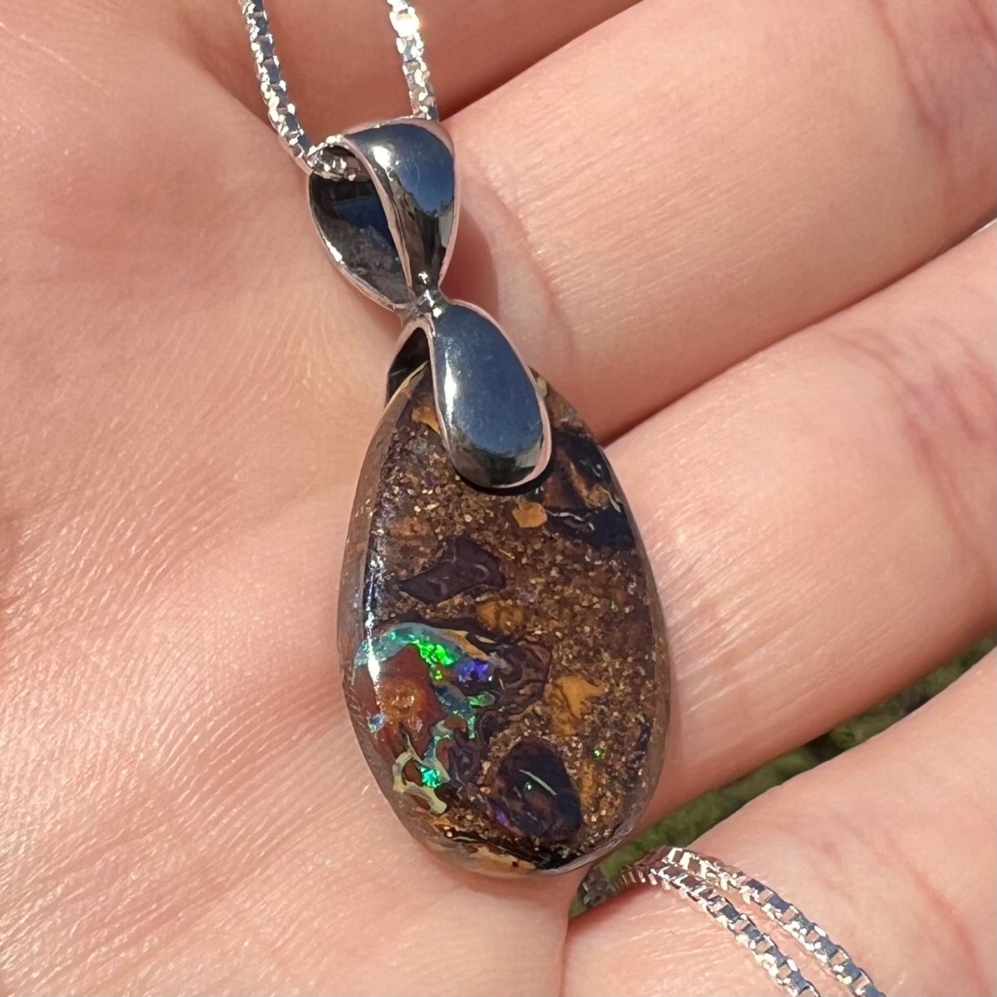 An Australian boulder opal necklace with a sterling silver bail. The opal has a bright green flash of color.