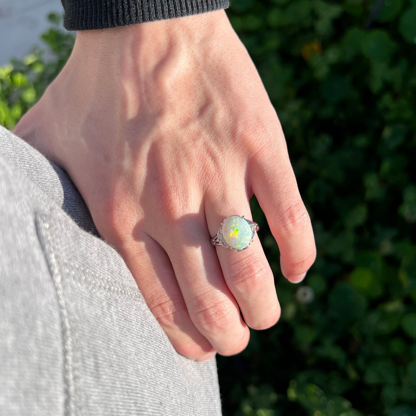 Close-up of hand resting on person's hip in natural sunlight wearing a women's natural 2.36ct opal ring with diamond accents in platinum.