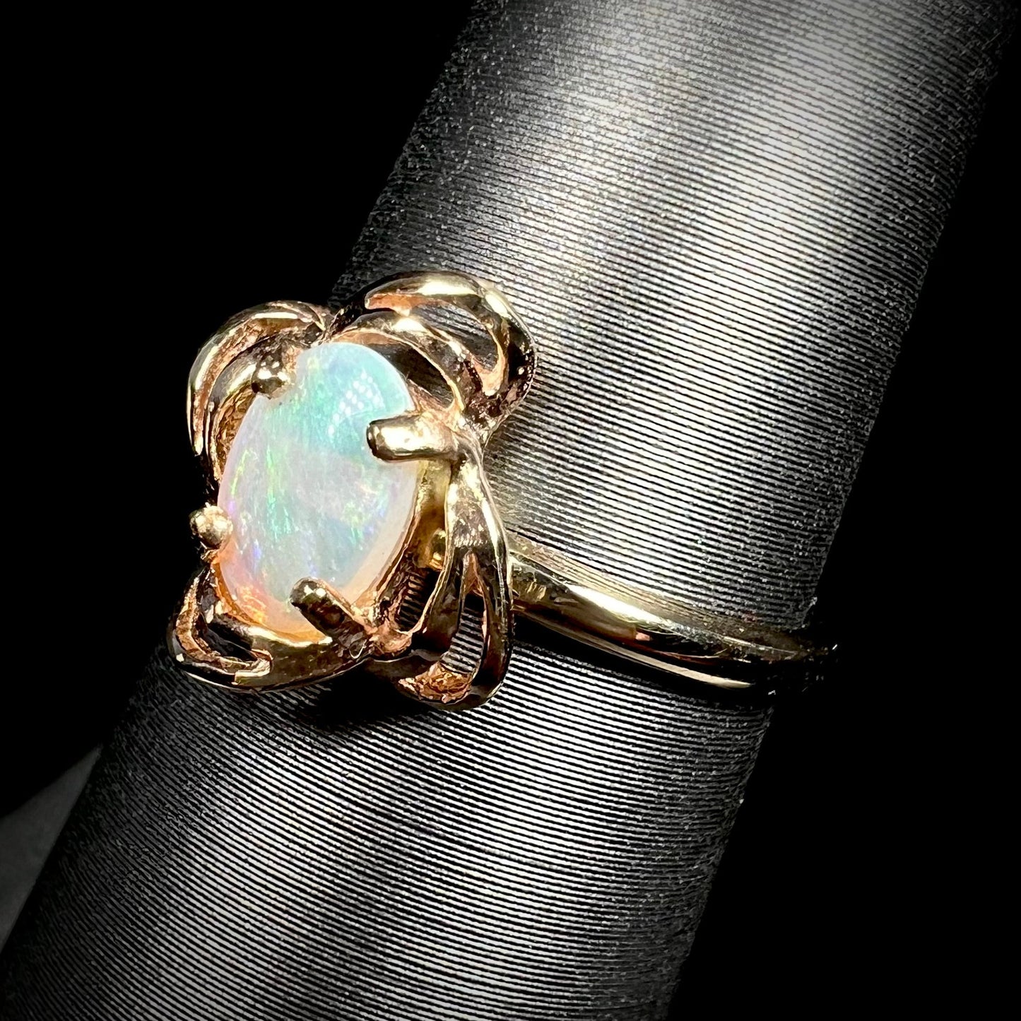 A yellow gold ring mounted with an oval cut opal. The opal has a white base tone with green and blue color play.