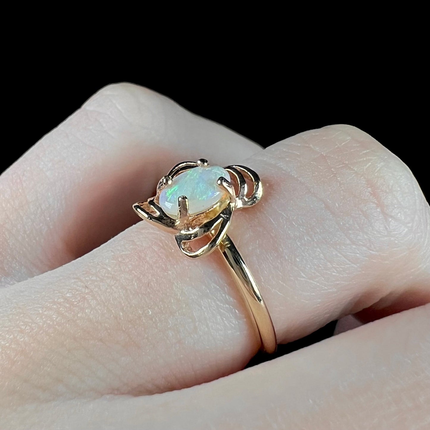 A yellow gold ring mounted with an oval cut opal. The opal has a white base tone with green and blue color play.