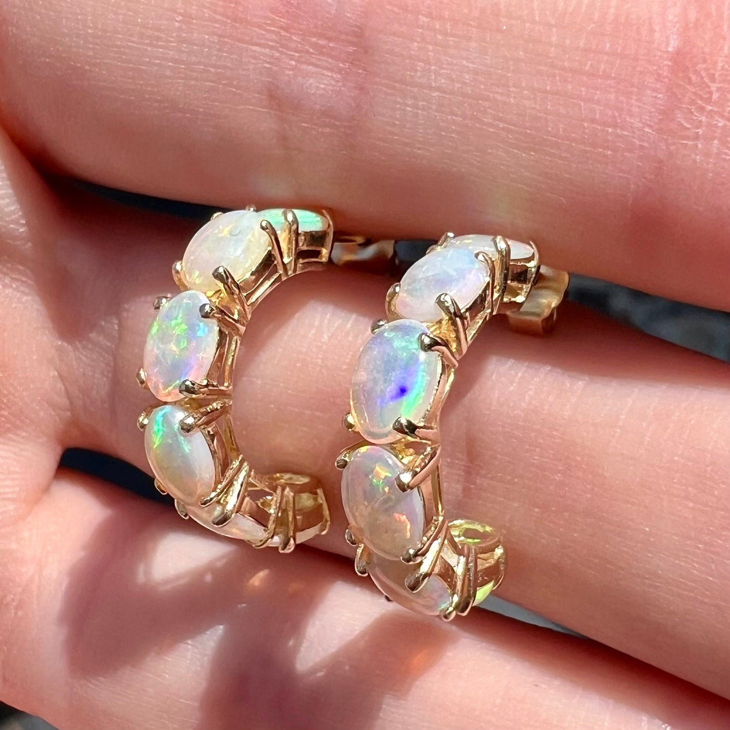A pair of yellow gold opal hoop earrings. Each earring is set with six natural oval cut opals.