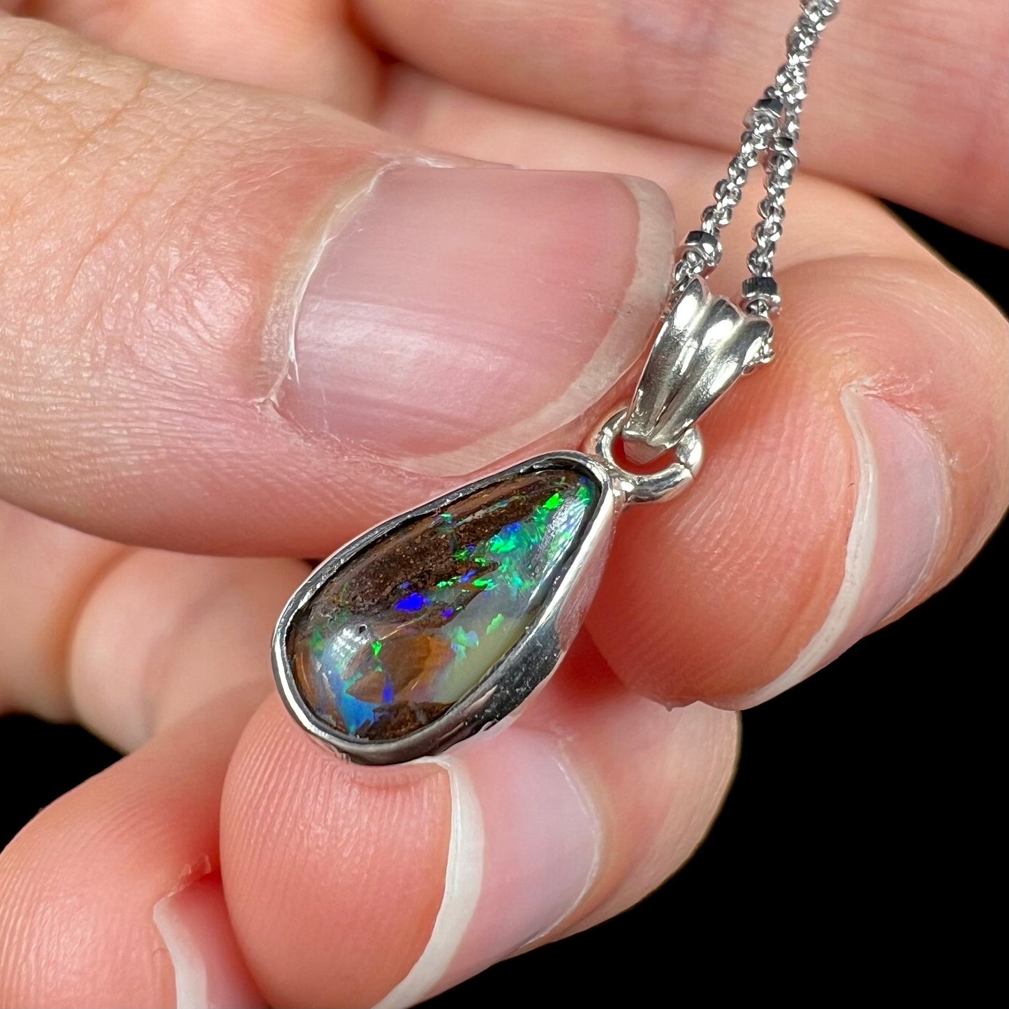 A natural, pear shaped Australian boulder opal with blue, purple, and green colors bezel set into a sterling silver necklace.