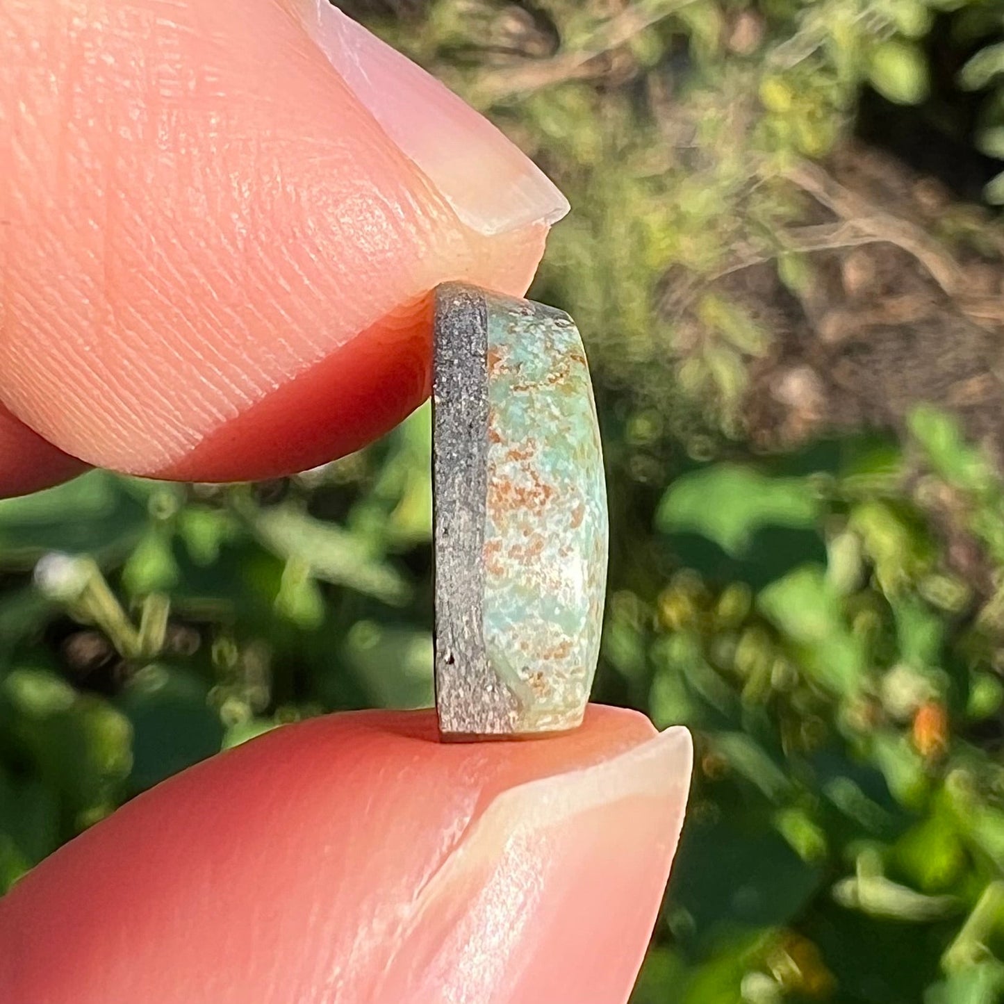 A loose, off-round cabochon cut turquoise stone. The stone is light blue with a red webbed matrix.