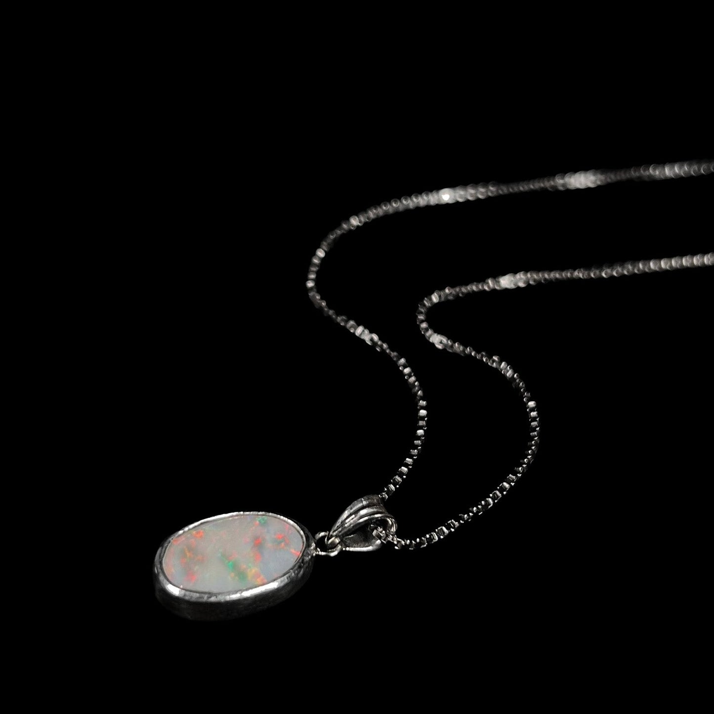A ladies' sterling silver necklace bezel set with a natural white crystal opal. The opal has red and blue fire.