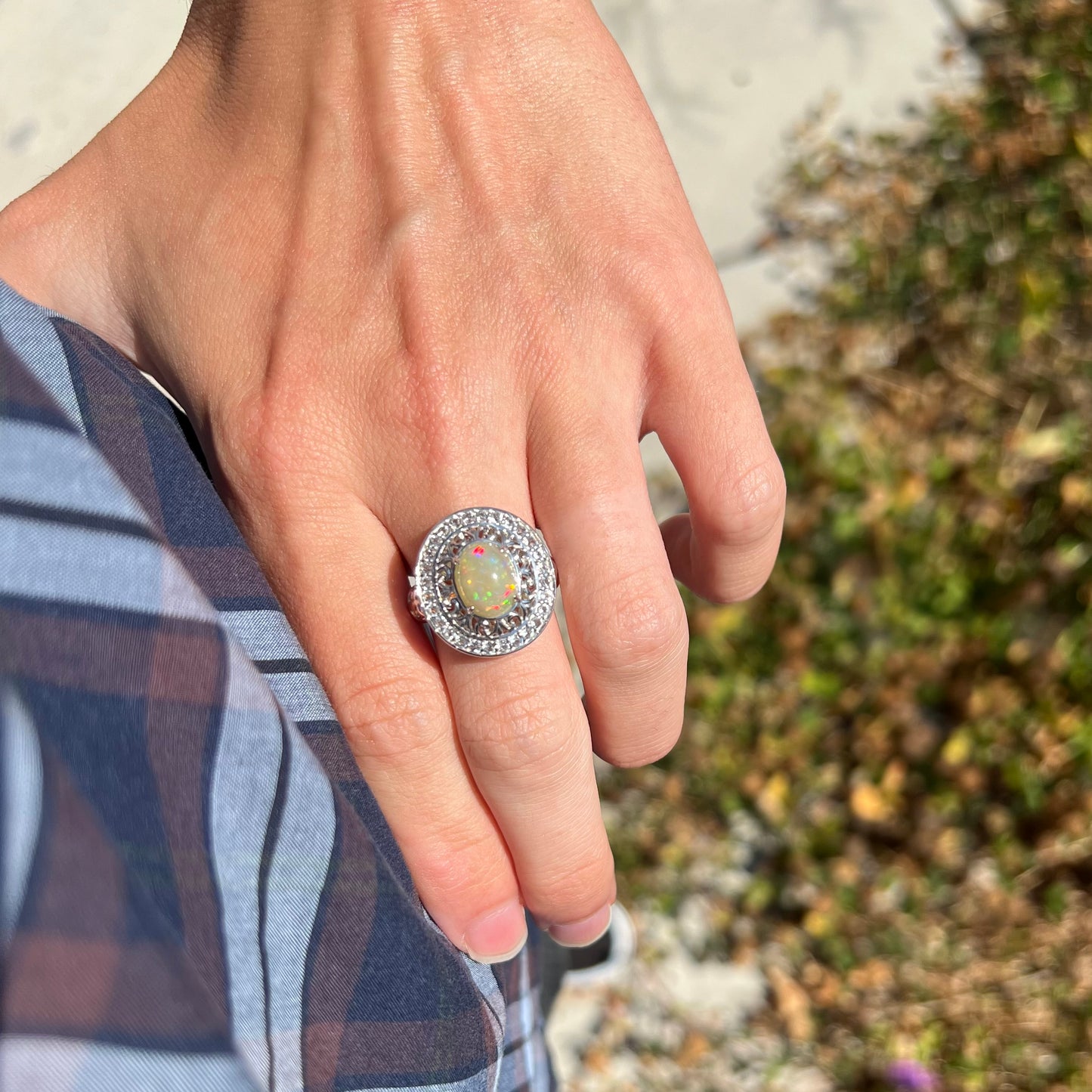 A big opal ring worn on a hand resting on a hip in the sunlight.