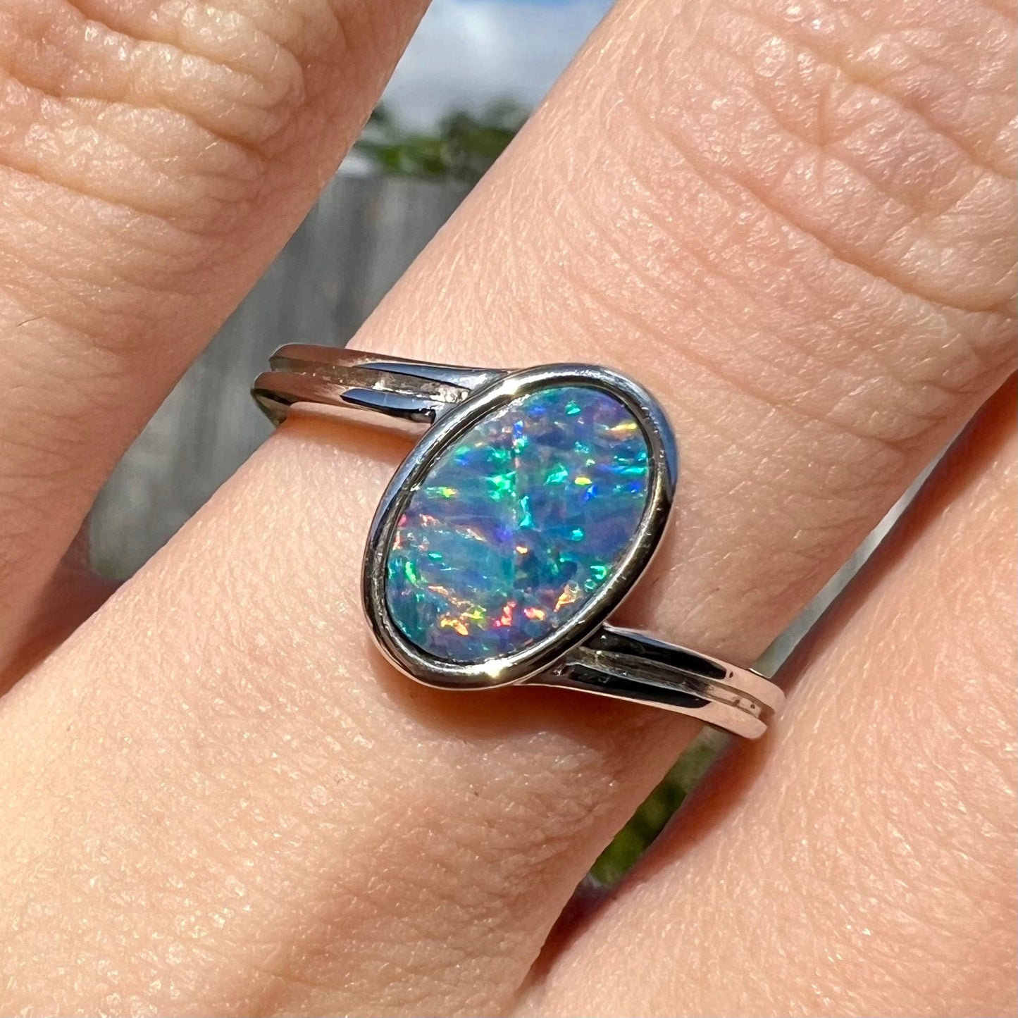 A sterling silver ring bezel-set with an oval shaped black opal doublet. The opal has red and blue fire.