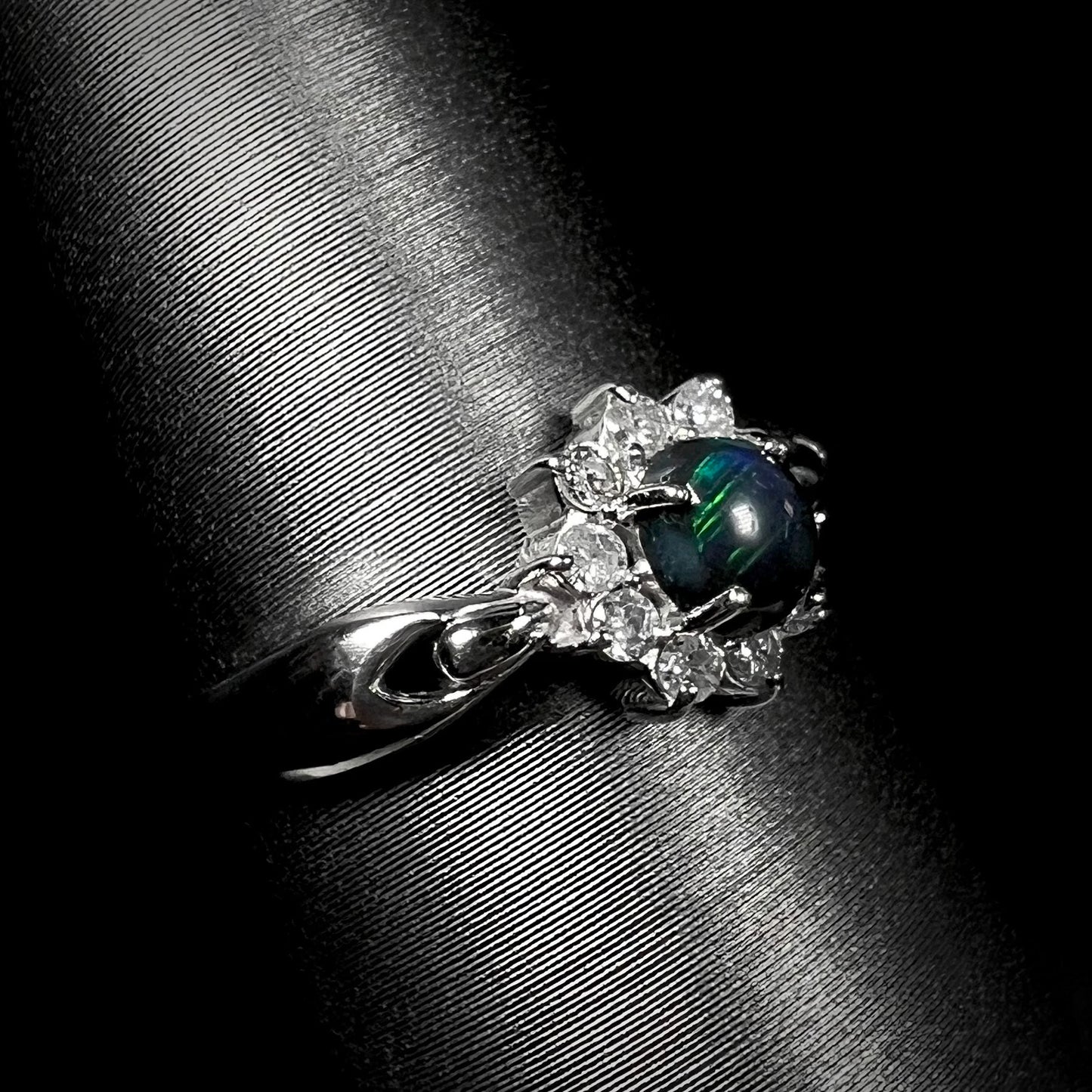 Angled view of opposite side of dainty black opal engagement ring with green color play.