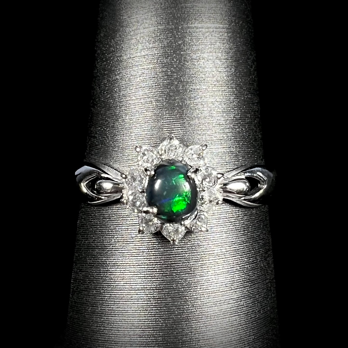 Front macro shot of black opal engagement ring with green flash, platinum setting, and diamond halo.