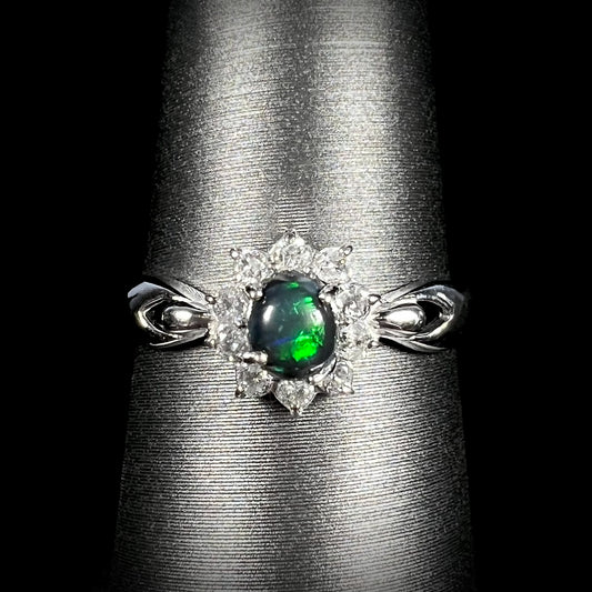 Front macro shot of black opal engagement ring with green flash, platinum setting, and diamond halo.